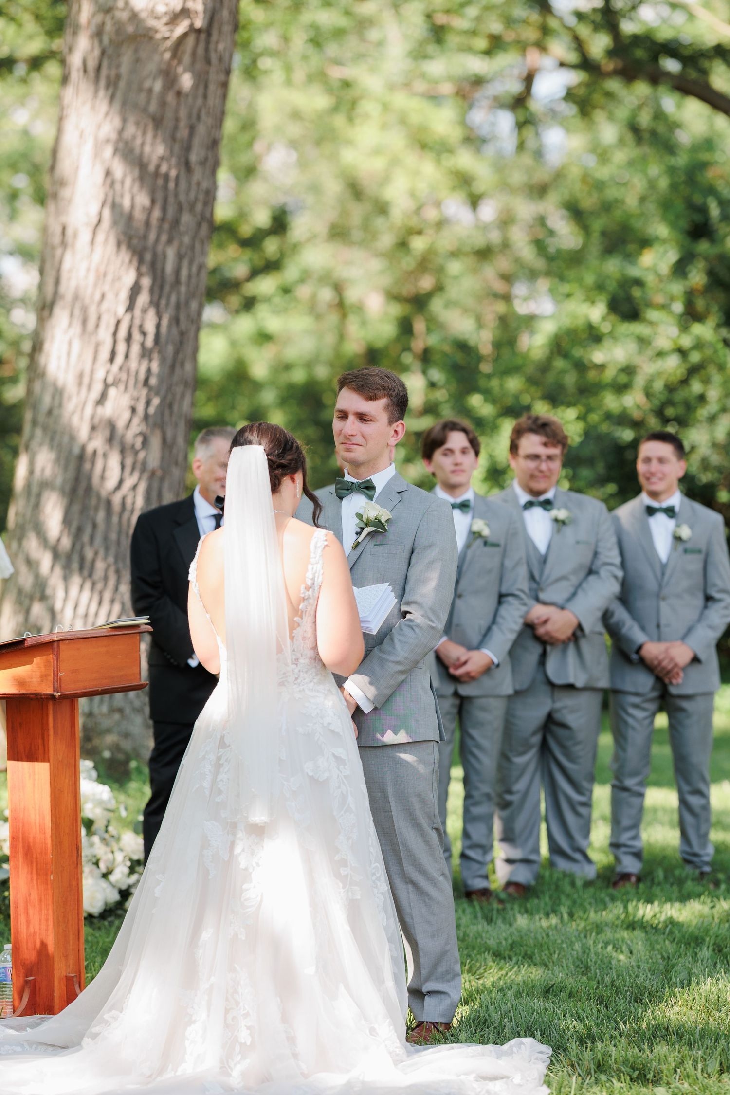 An outdoor wedding ceremony with groomsmen in gray suits watching the couple's first look.