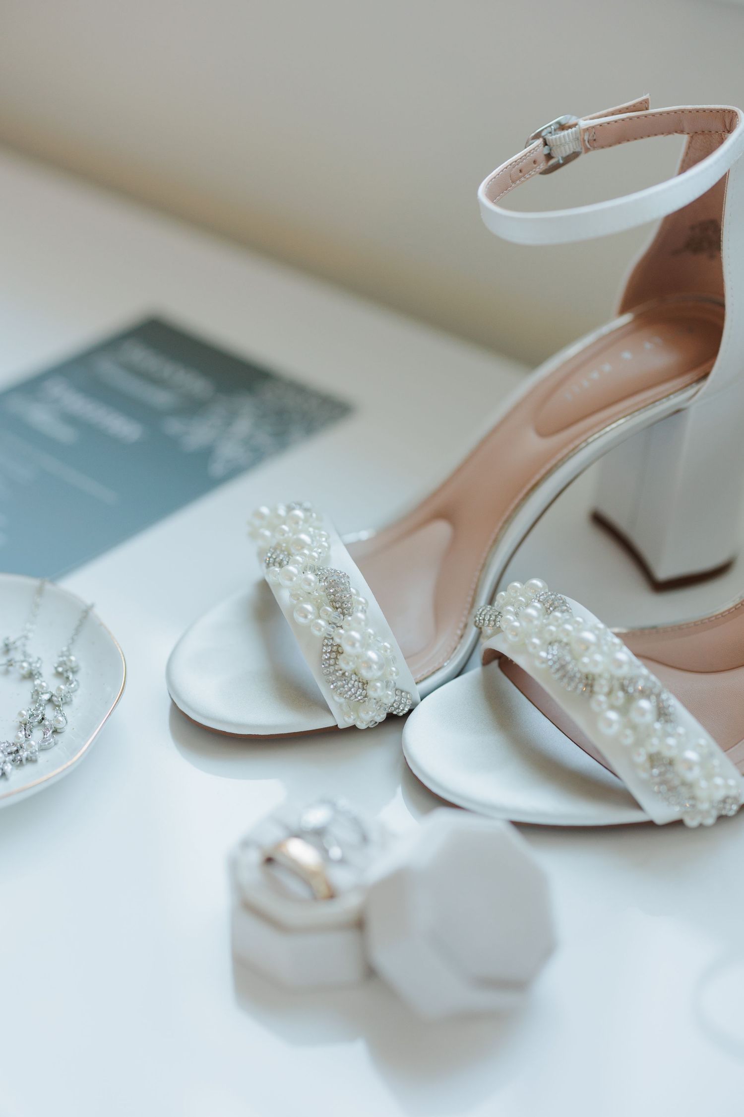 Elegant white bridal shoes with pearl embellishments displayed on a light surface.