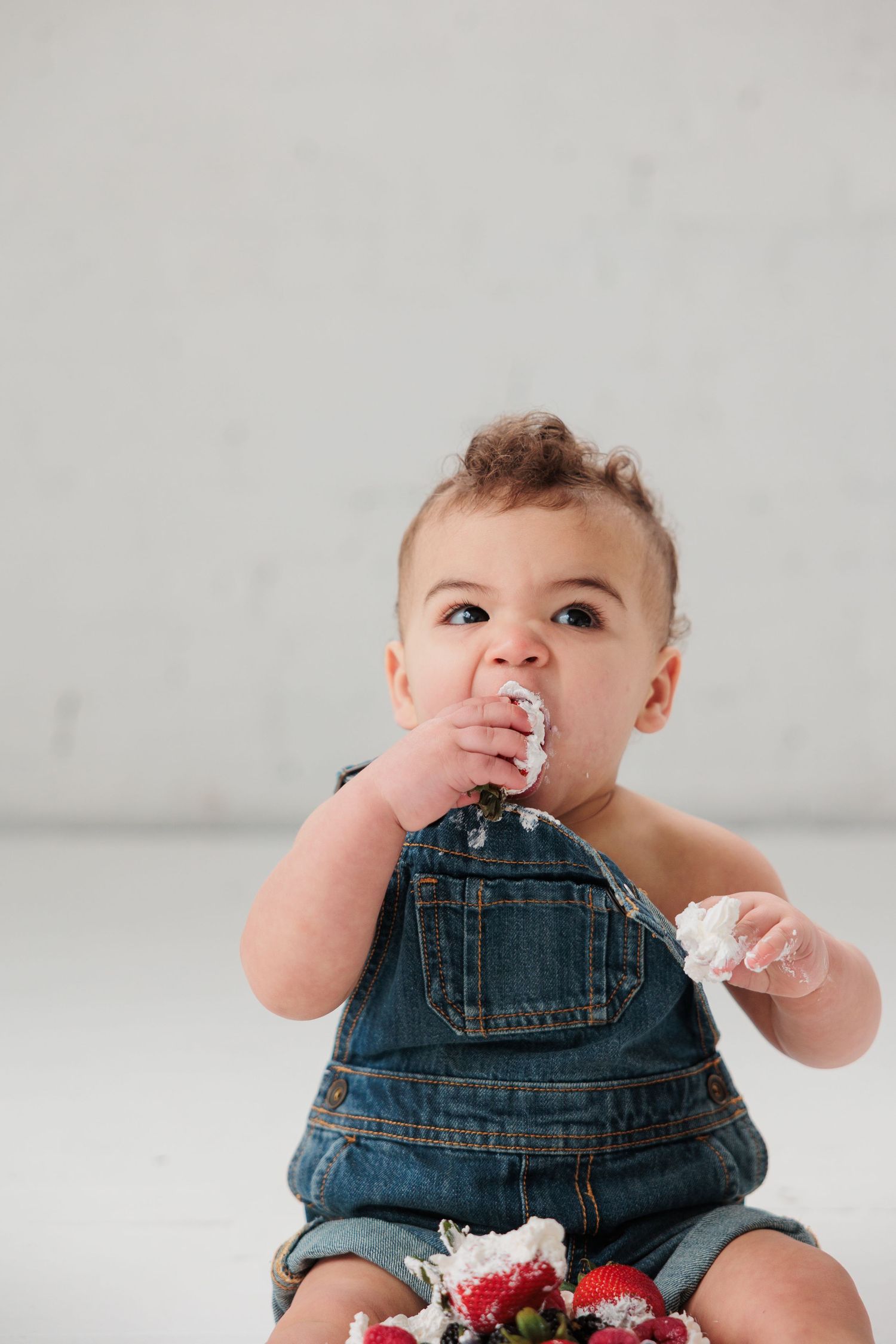 A messy-faced baby in denim overalls eats fresh berries and whipped cream.

Rochester NY wedding photographer