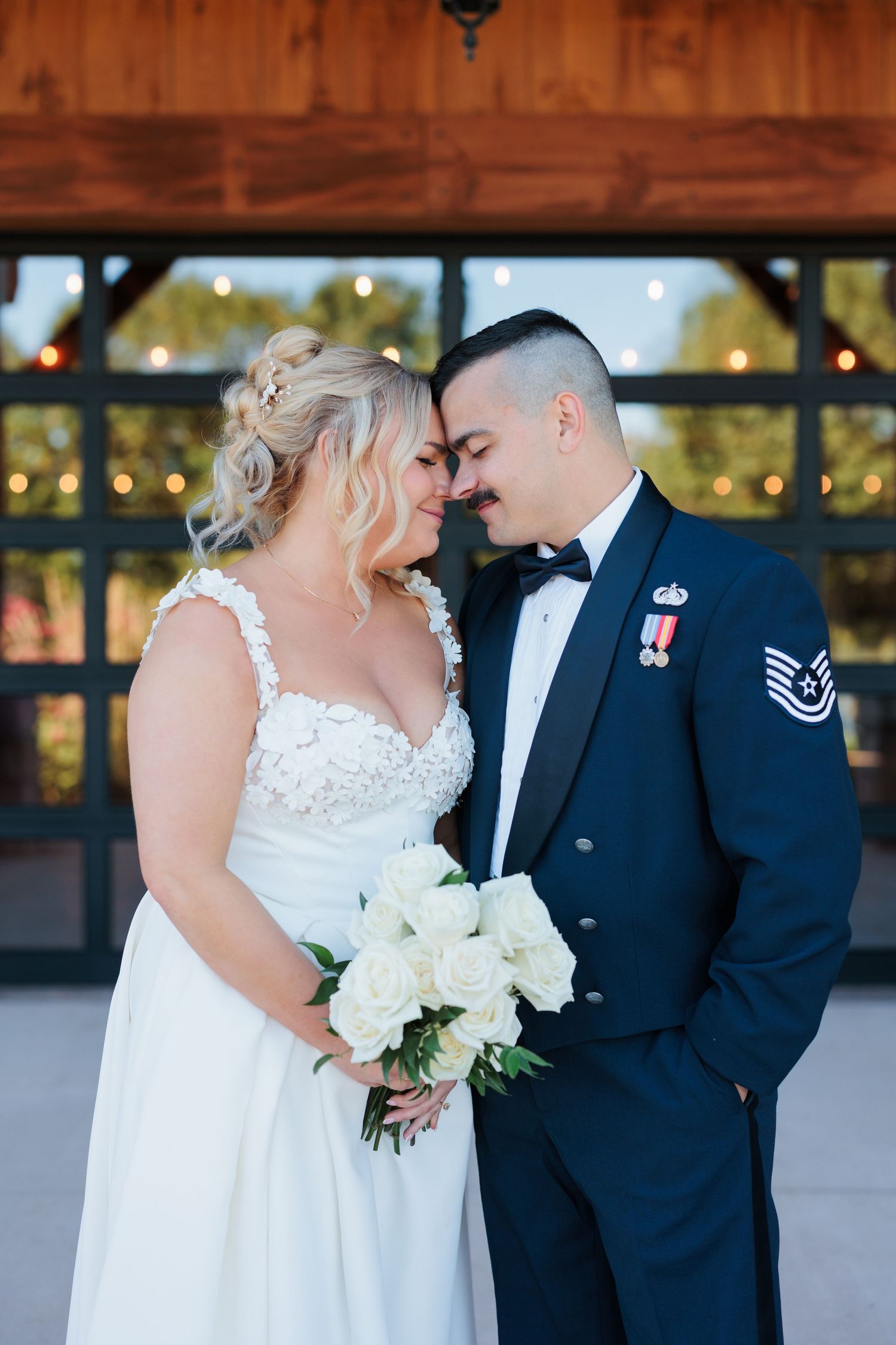 A romantic wedding couple sharing intimate kisses while wearing a white dress and military uniform in an outdoor setting.