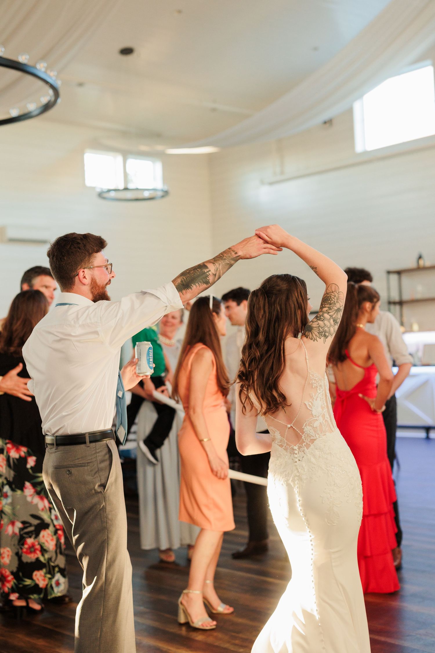 Bride and groom share a joyful dance at their wedding reception, surrounded by guests in a bright, elegant venue.