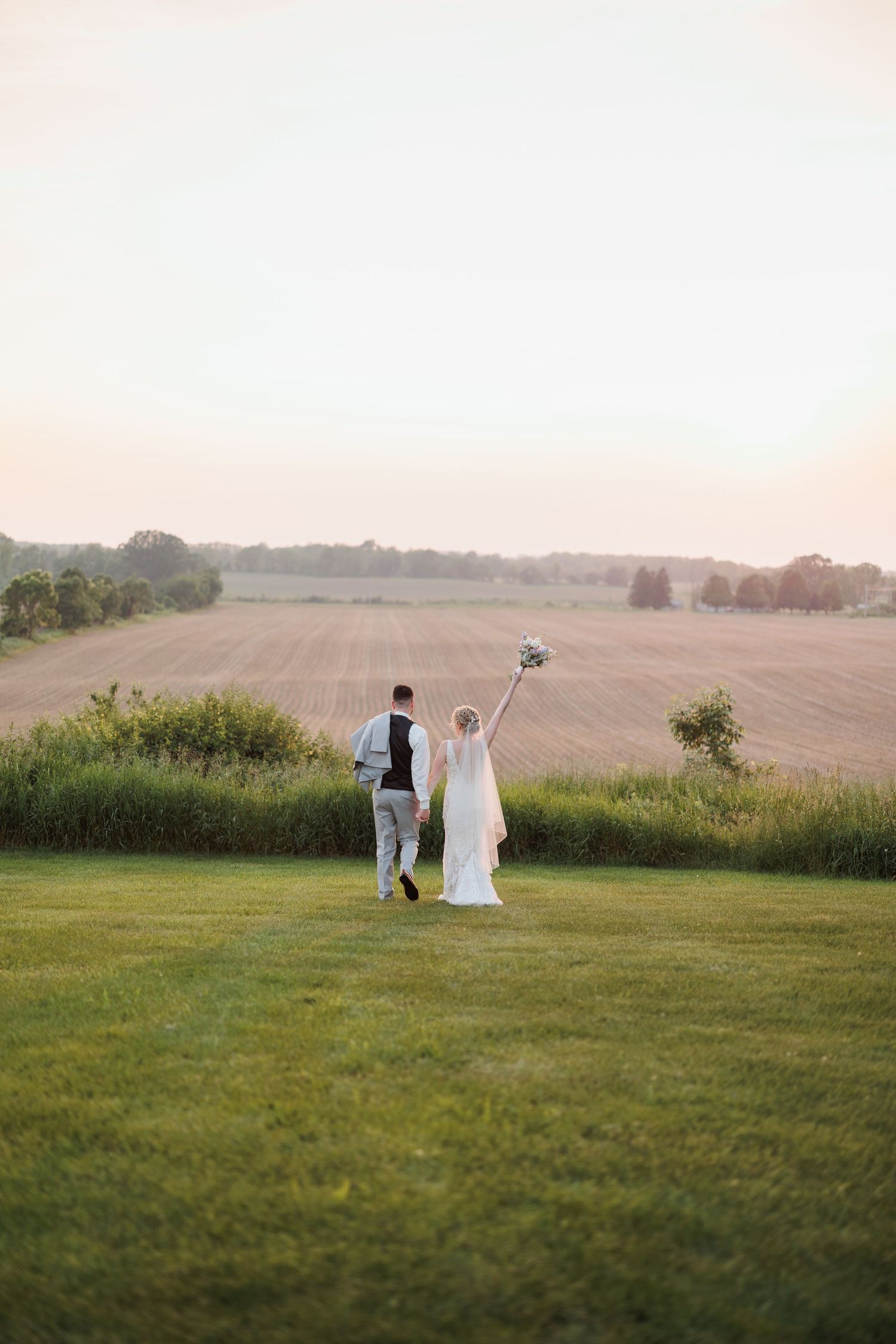 Wedding couple silhouetted against sunset in peaceful countryside setting.