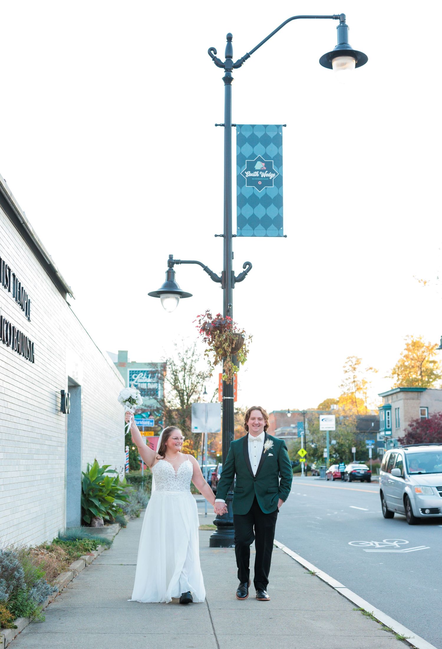 Wedding couple walking along small town sidewalk with blue vintage lampposts.