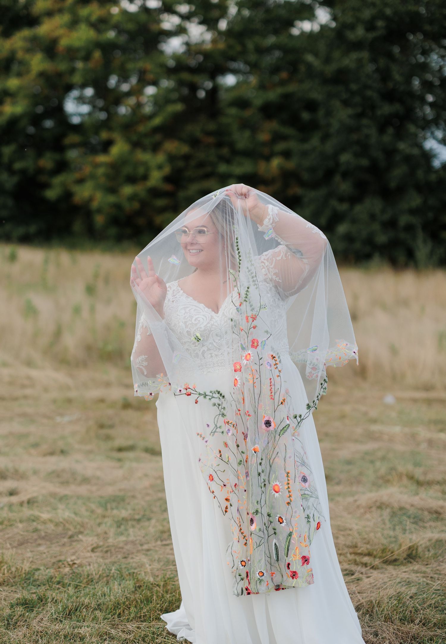 A delicate floral embroidered wedding veil with coral and pink flowers lays displayed in a field.