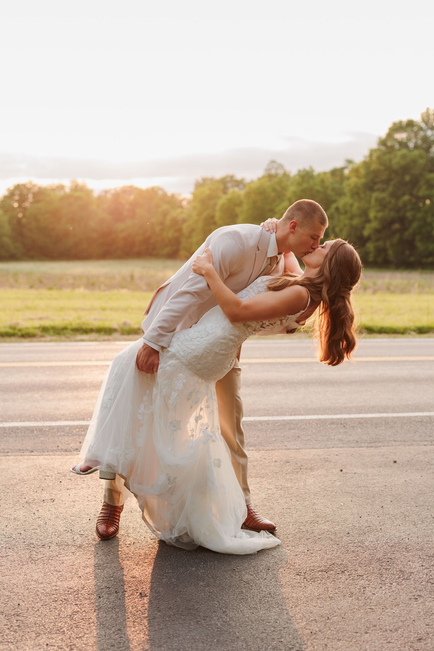 A romantic sunset dip pose between newlyweds in a parking lot.