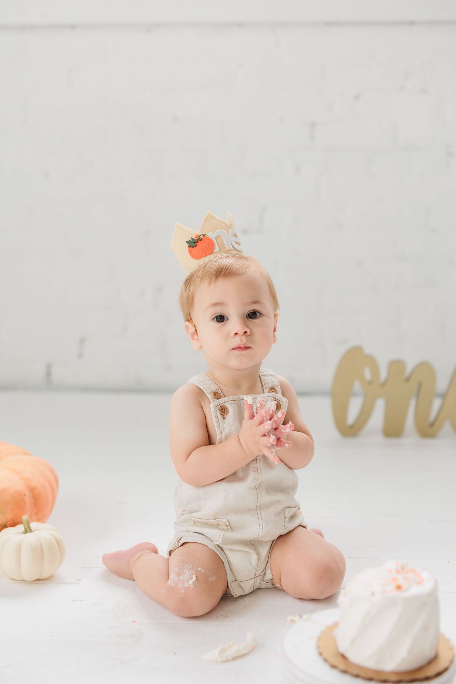 Baby in beige romper sitting with pumpkins and cake during first birthday photoshoot.

Rochester NY wedding photographer