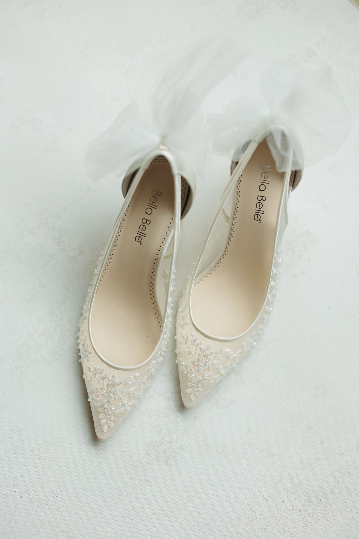 Delicate white lace bridal flats displayed on a light background.