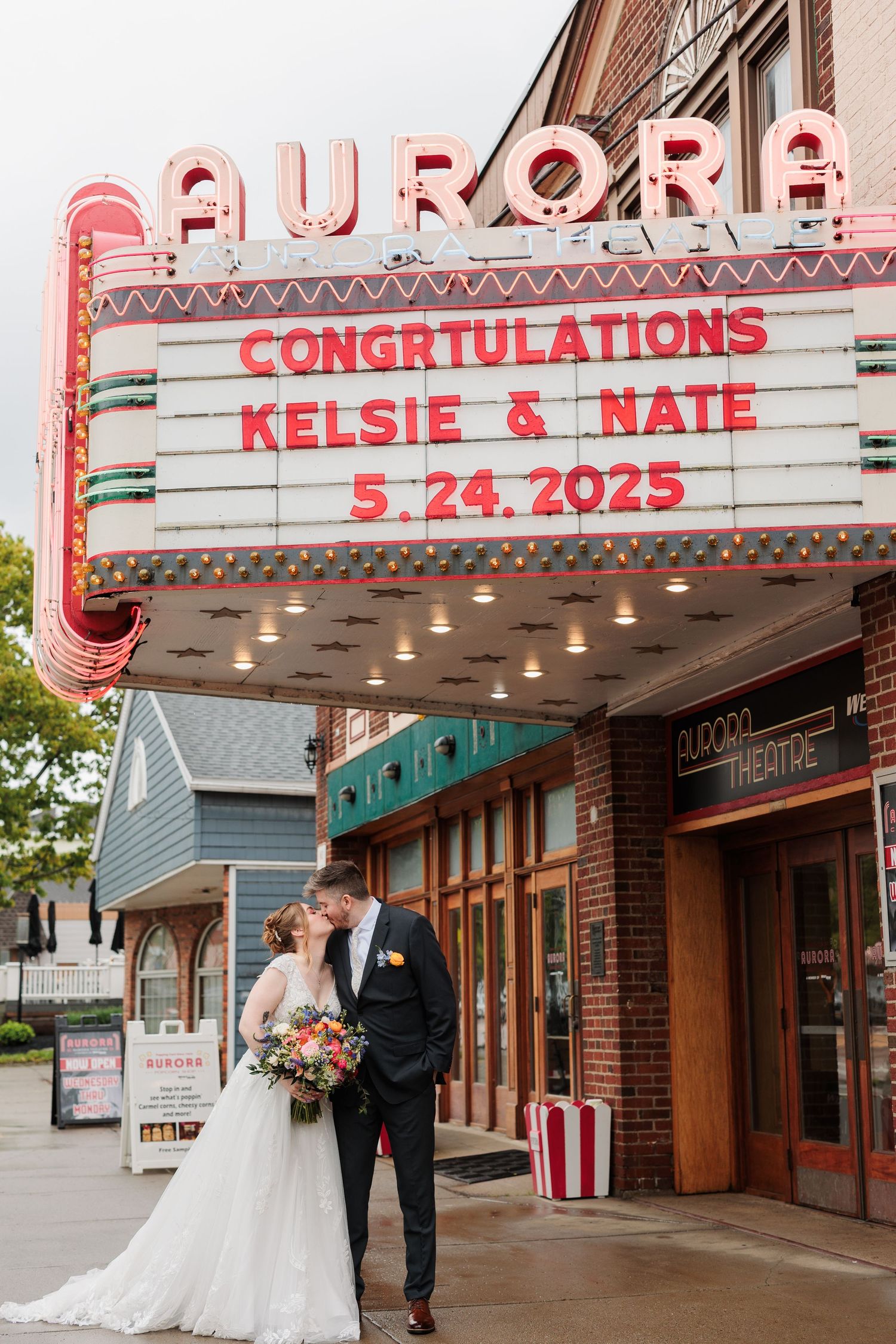 A wedding couple poses outside a vintage movie theater with congratulatory marquee signage.