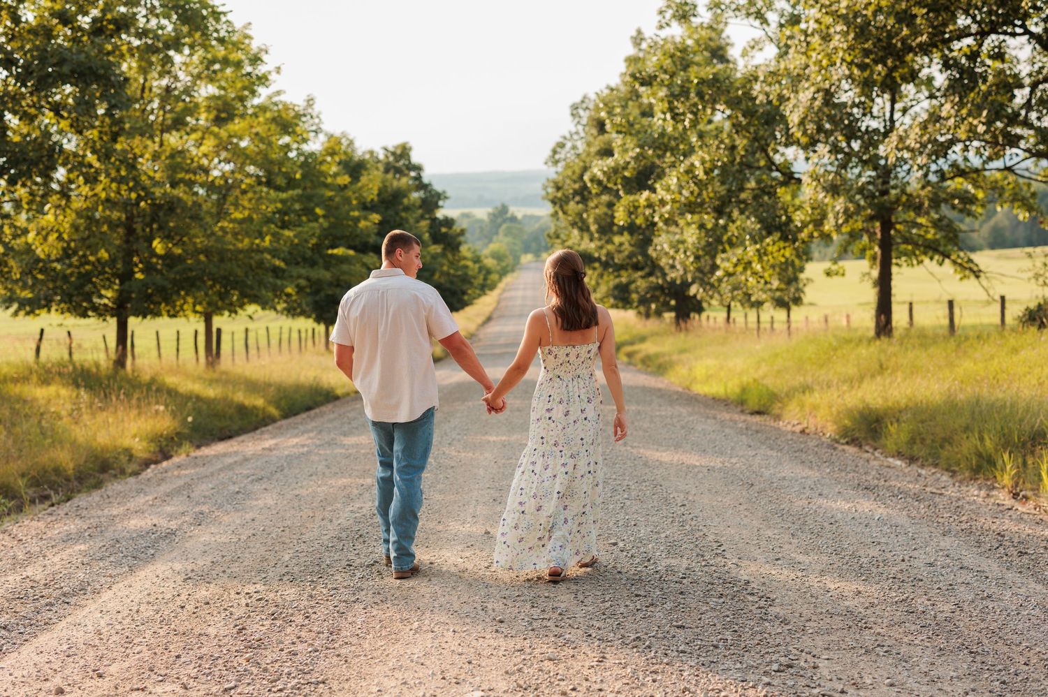Couple walks together on rural gravel road during golden hour photoshoot.