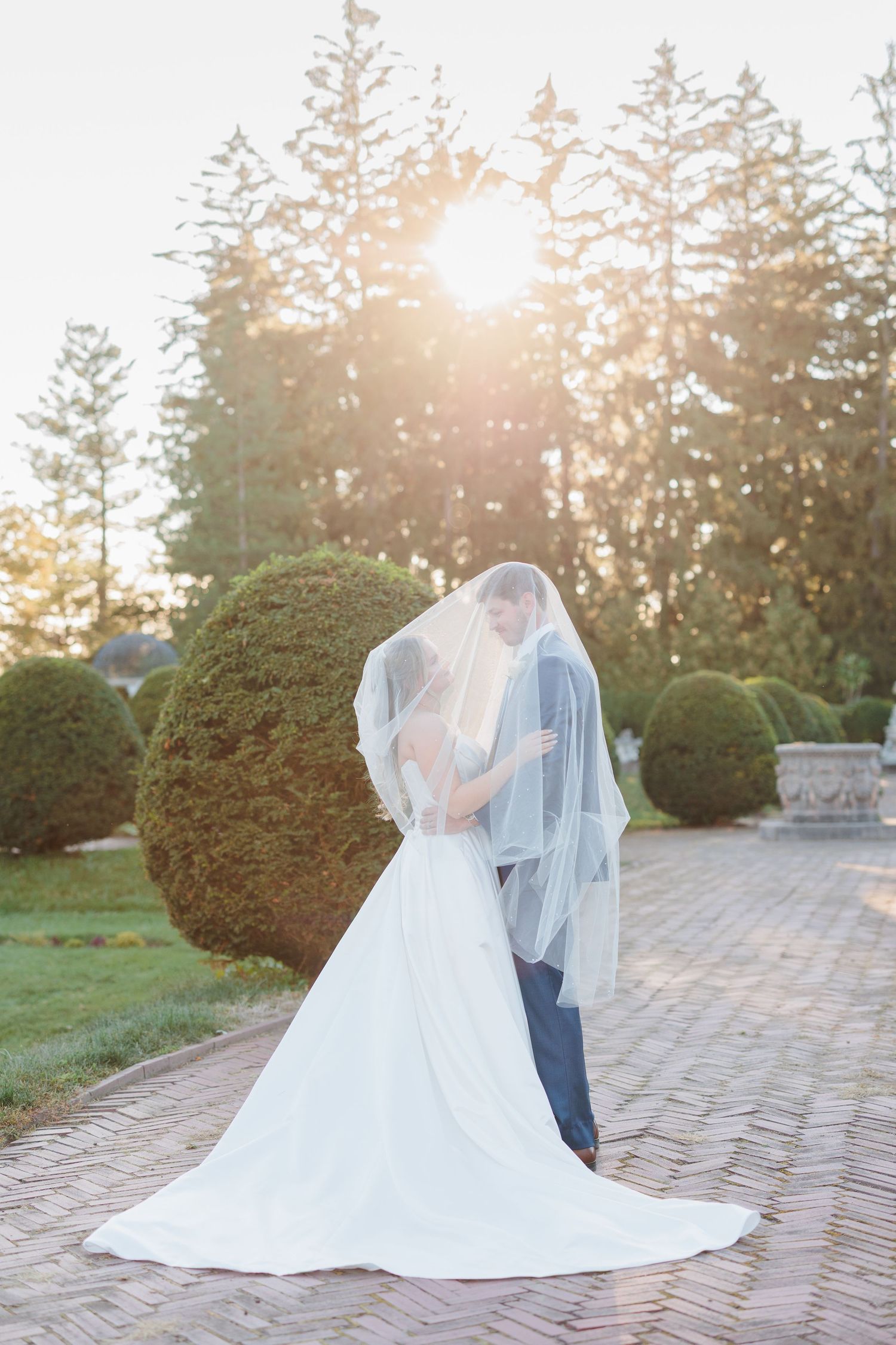 Romantic wedding couple embracing on stone path surrounded by manicured gardens at sunset.

Rochester NY wedding photographer