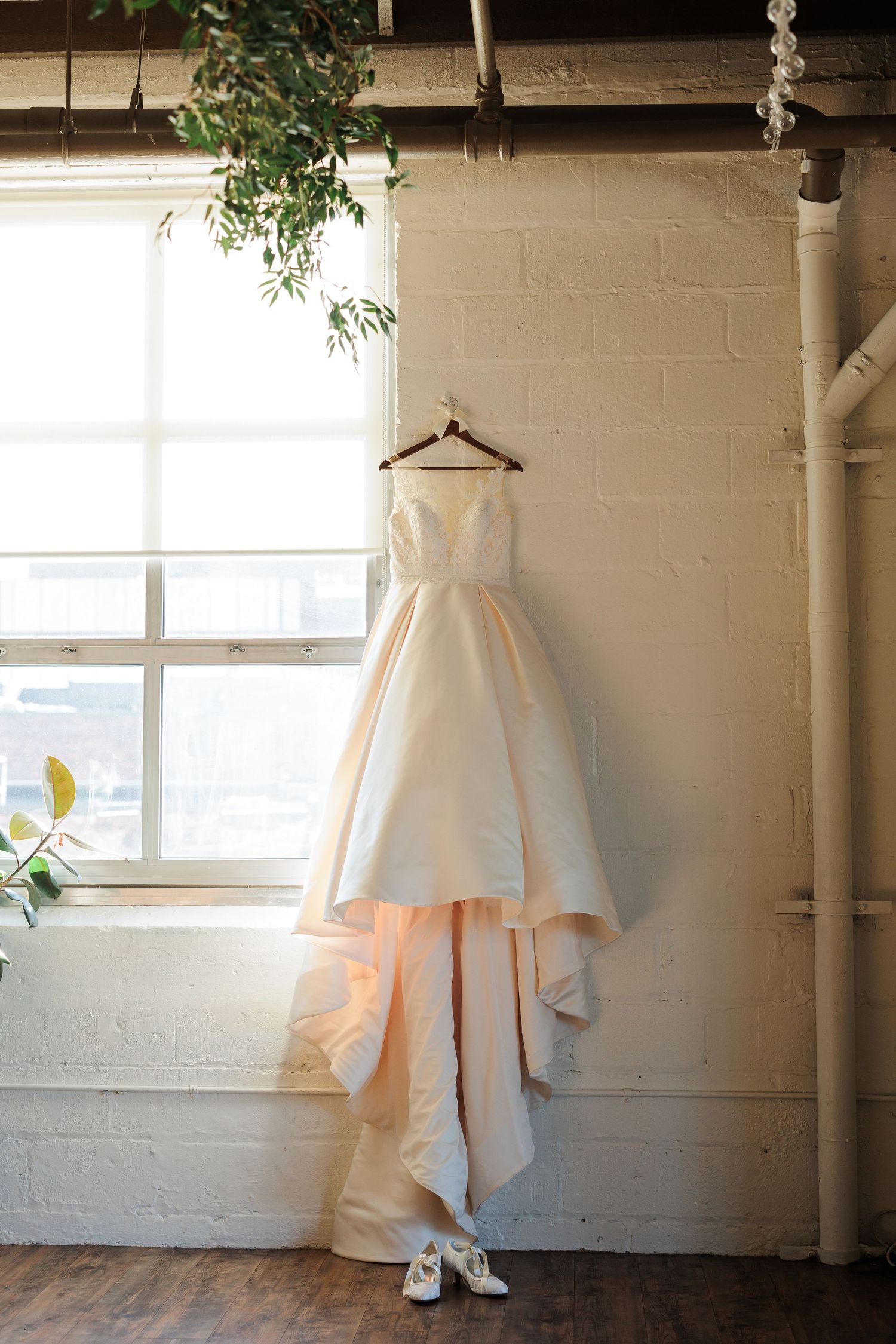 White wedding dress displayed against white brick wall with natural window light.