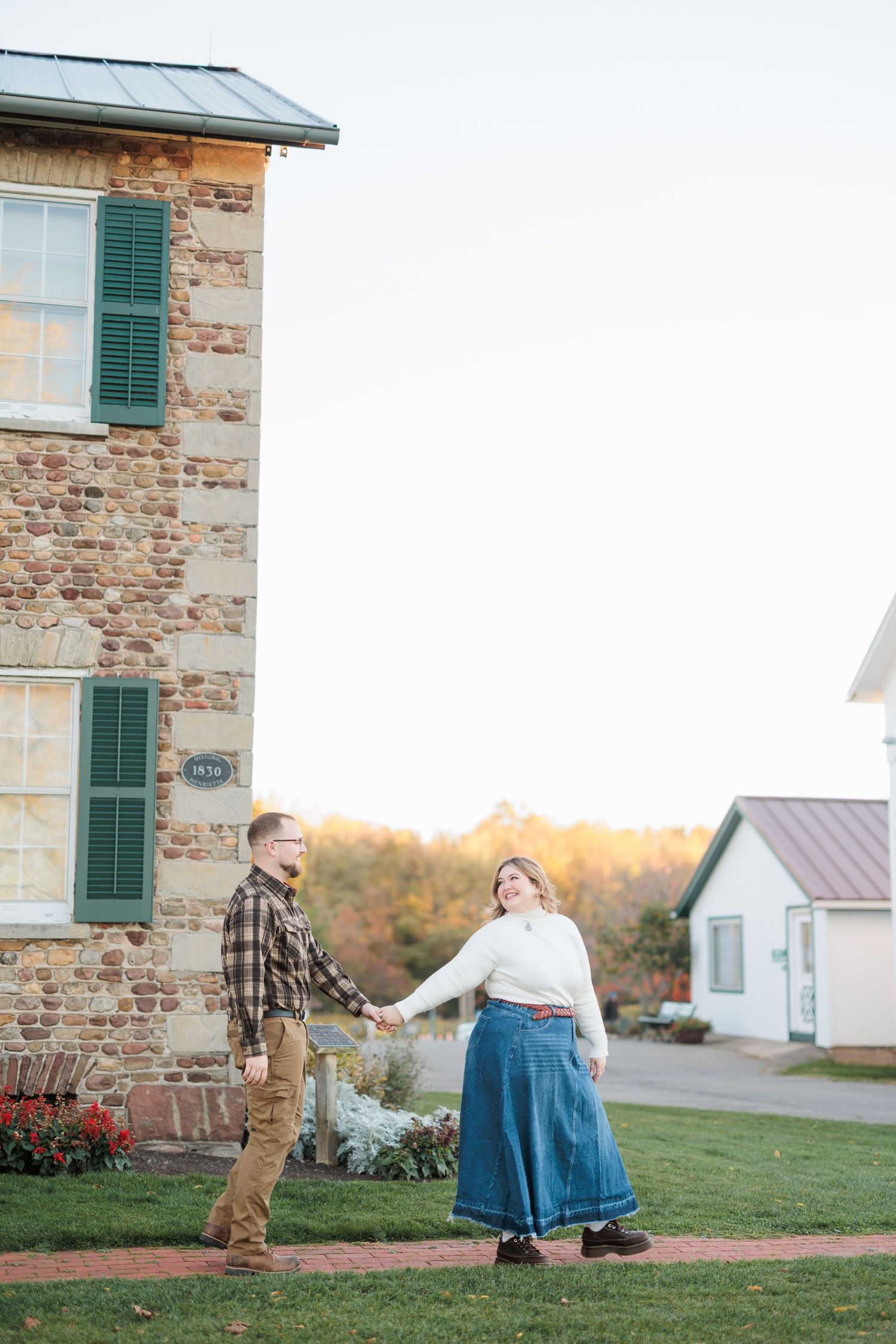 Couple dancing and twirling together at sunset outside a rustic stone building with green shutters.