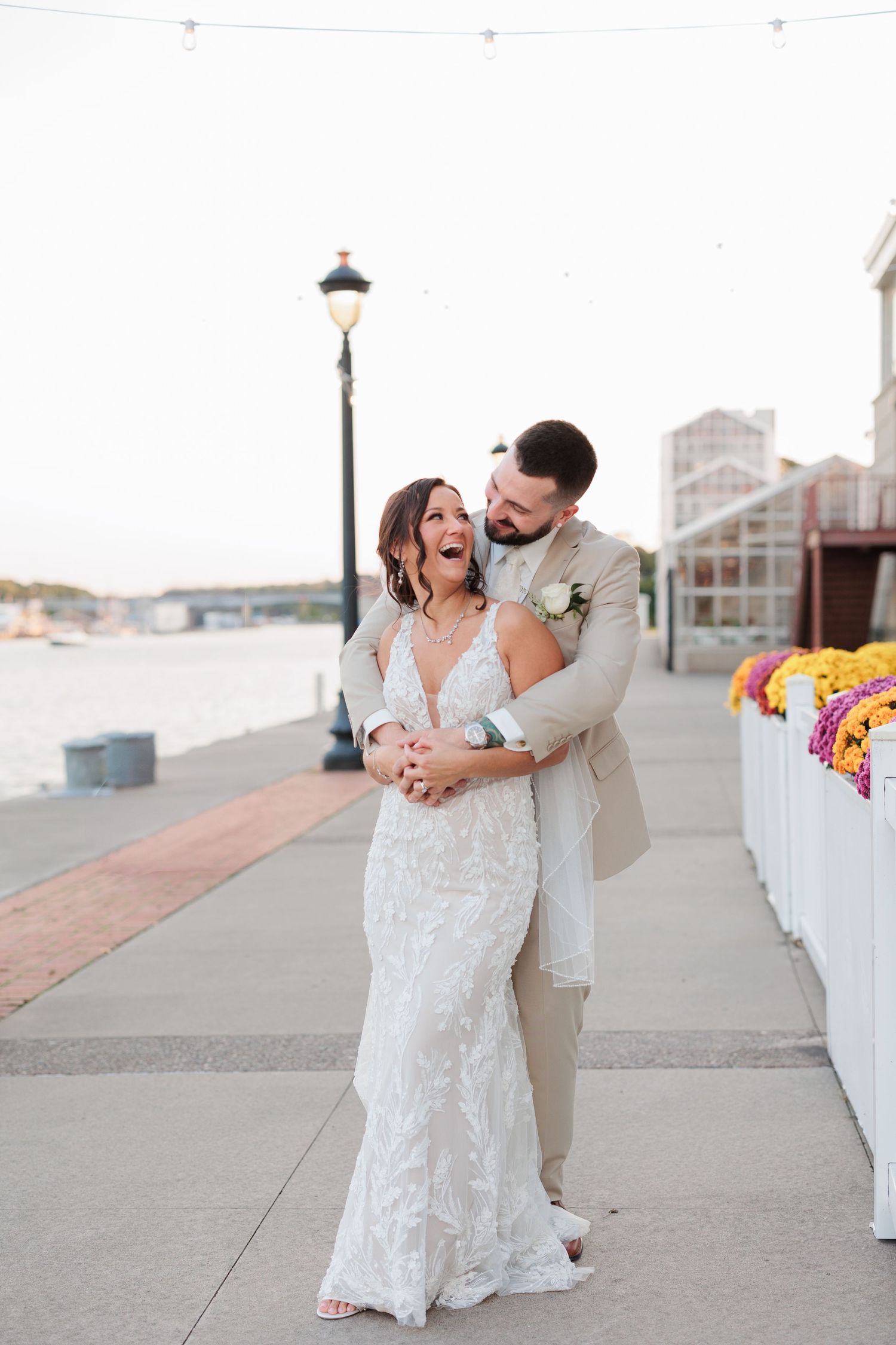 A happy couple embraces and laughs together on a waterfront boardwalk.