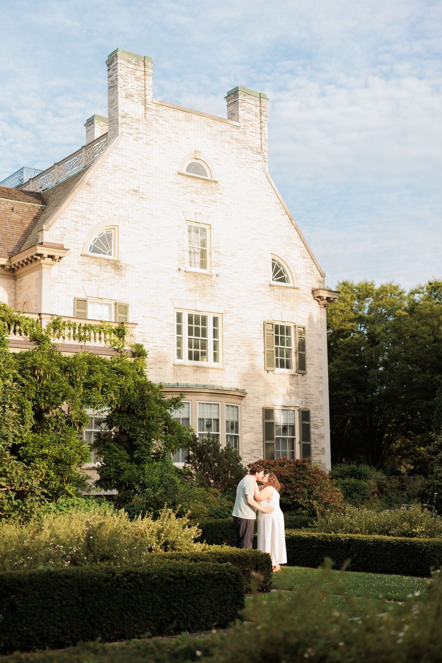 A romantic portrait in front of a historic white mansion with manicured hedges.
