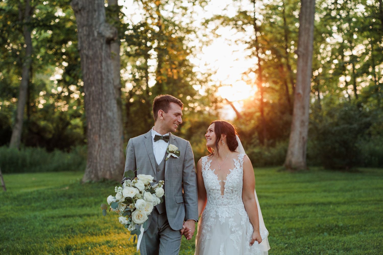 A wedding couple embraces in a golden sunset with trees and natural scenery in the background.