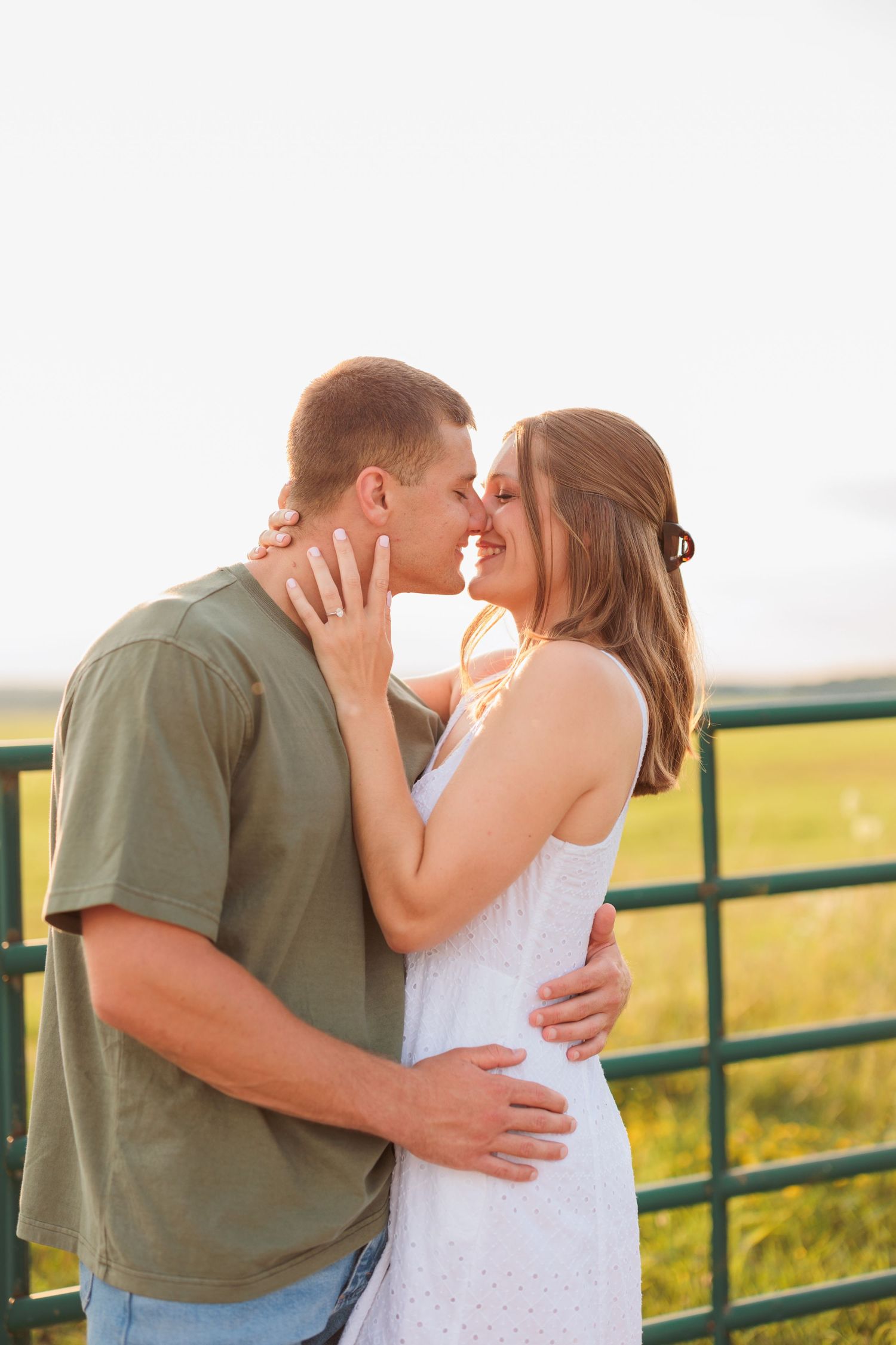 Intimate couple shares tender moment against rustic farm fence at sunset.