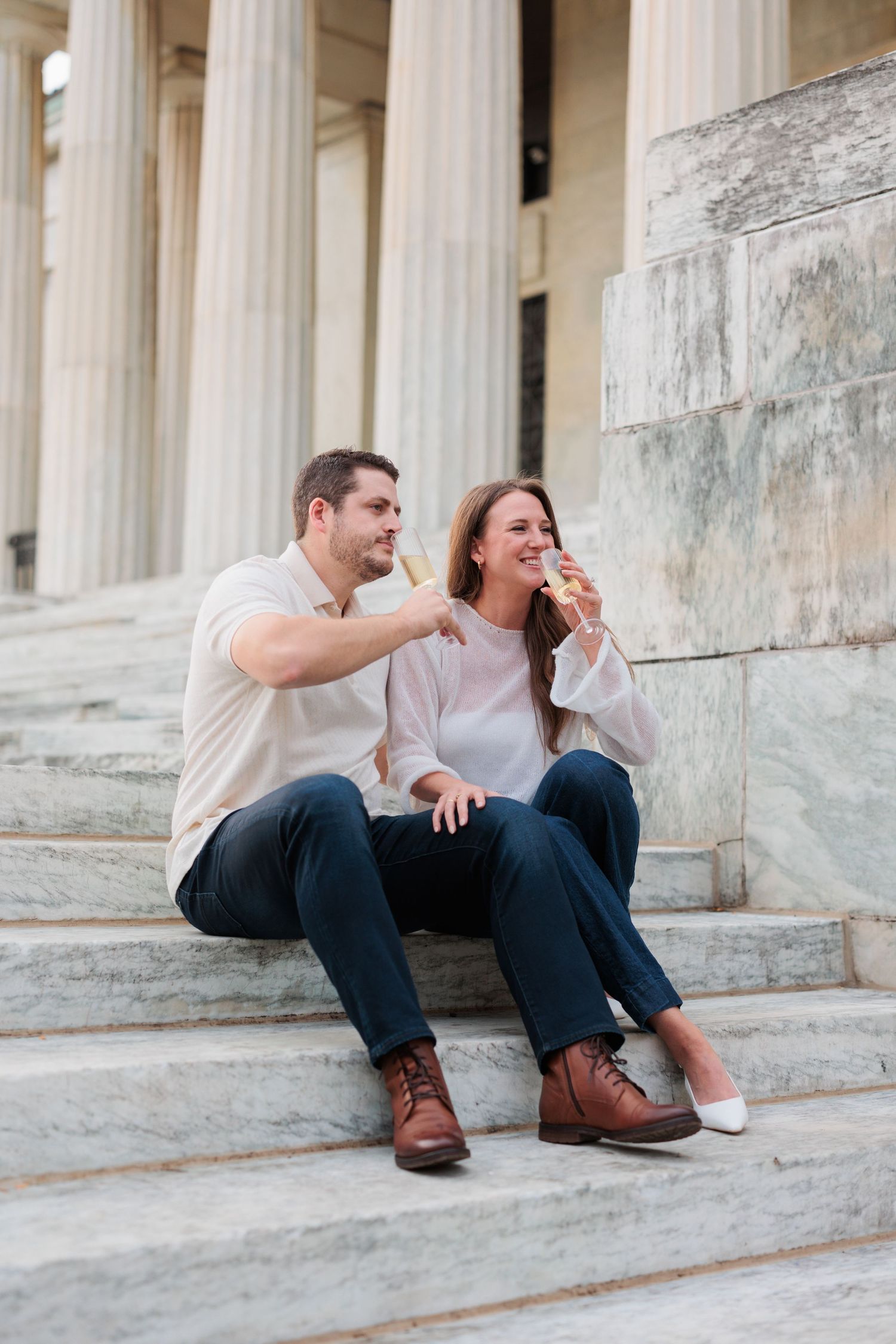A couple sharing a lighthearted moment while sitting on stone steps with classical columns in the background.