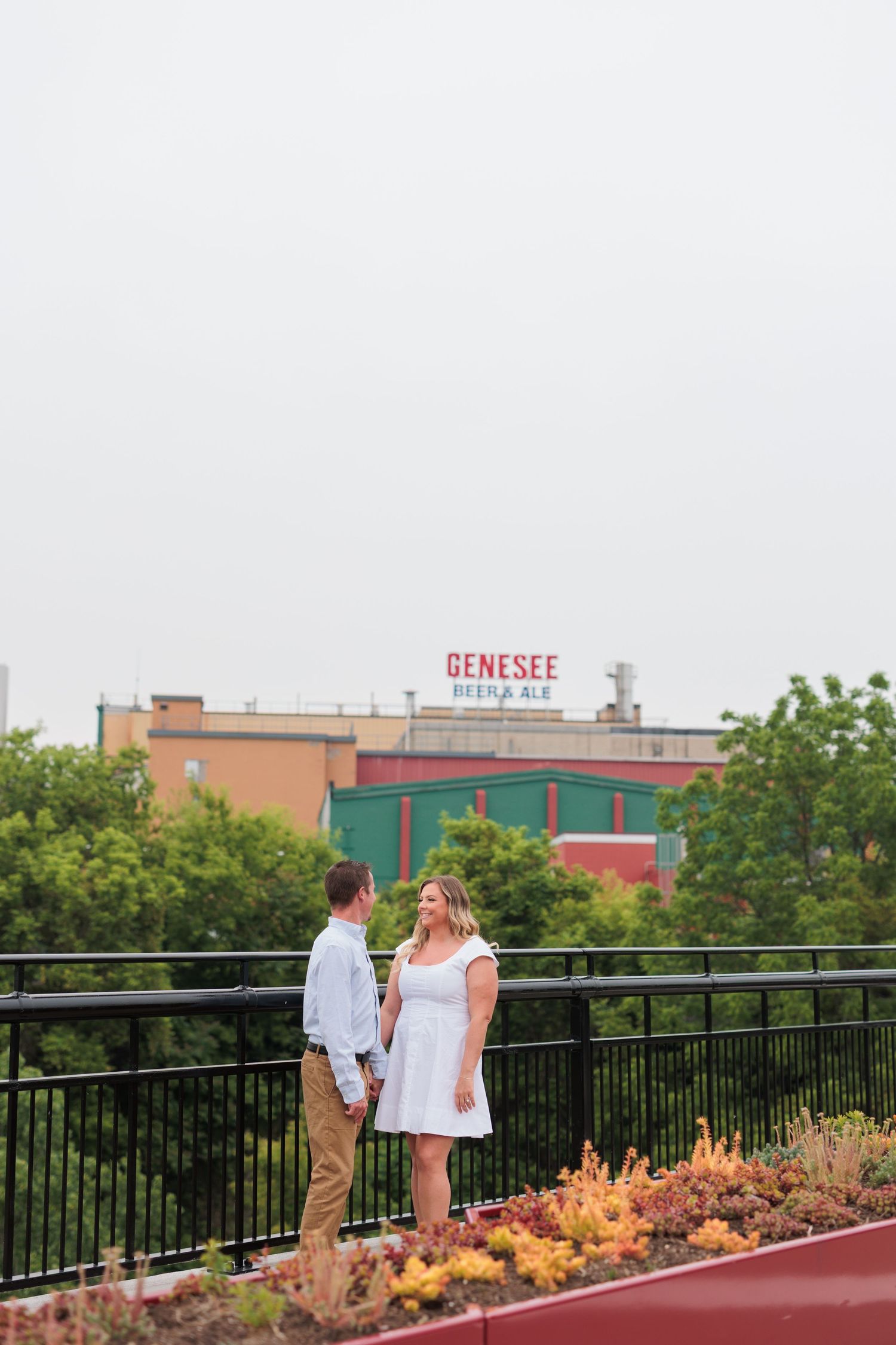 A couple poses on a rooftop garden with the Genesee building sign visible in the background.