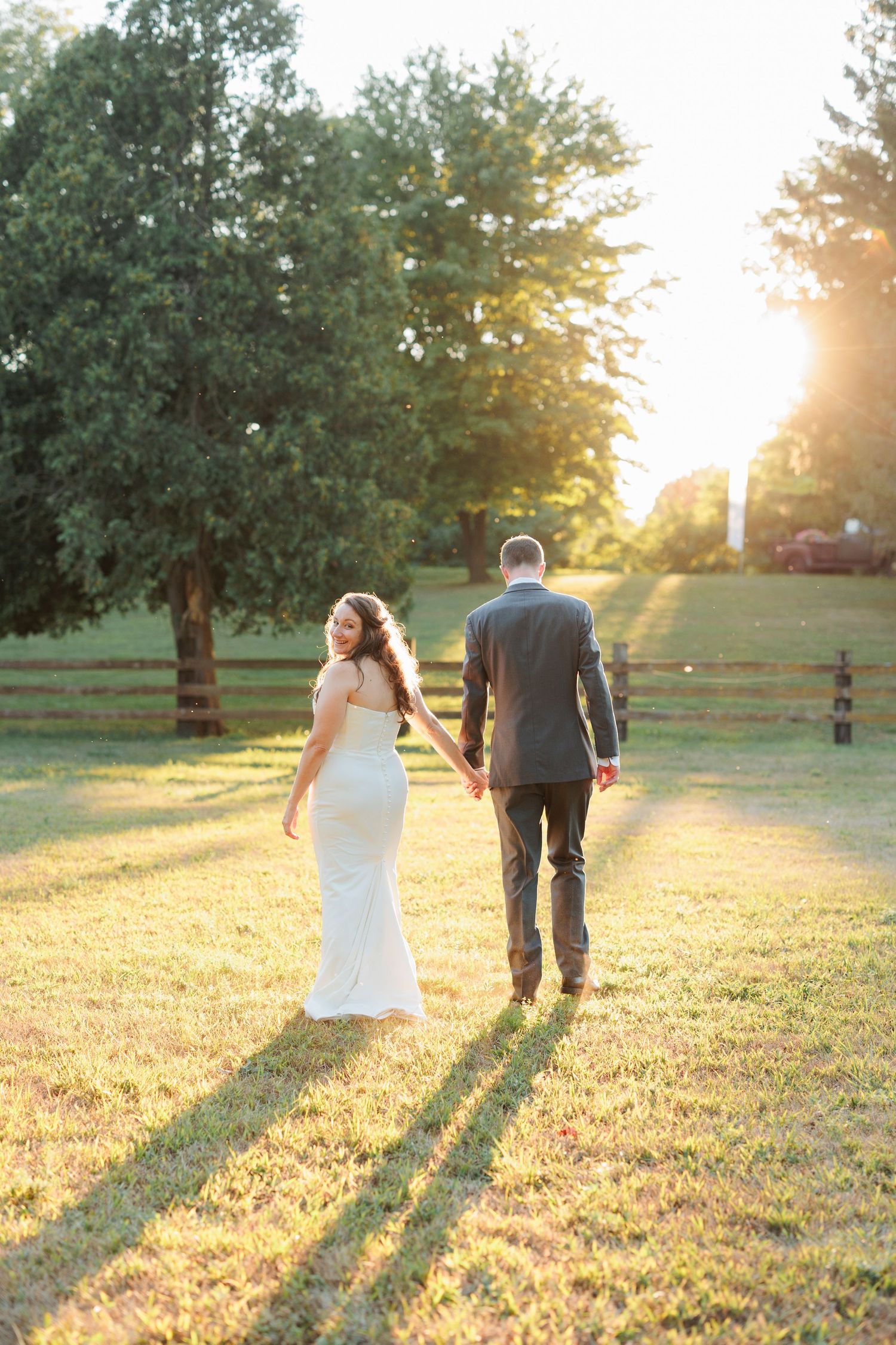 A couple walks away into the sunset creating long shadows across a grassy field.