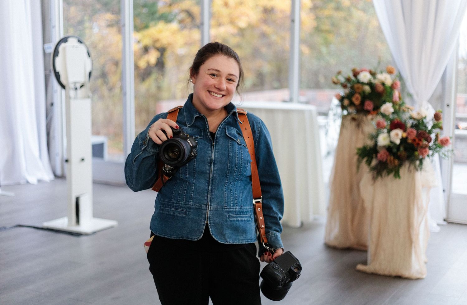 A person in denim attire stands in an elegant white event venue with floral decorations and sheer curtains.