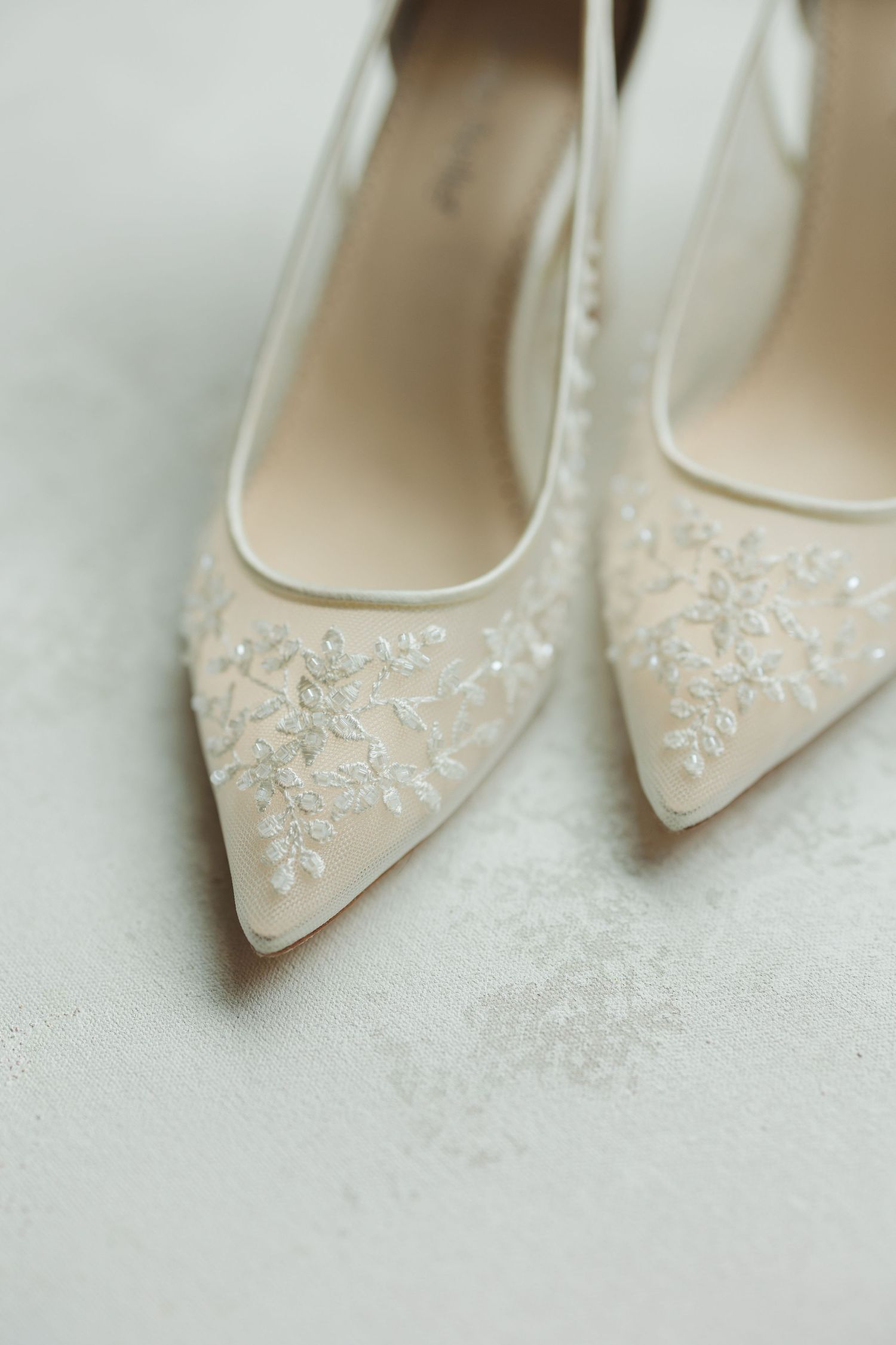 Elegant bridal shoes with delicate lace embroidery details photographed in soft focus.