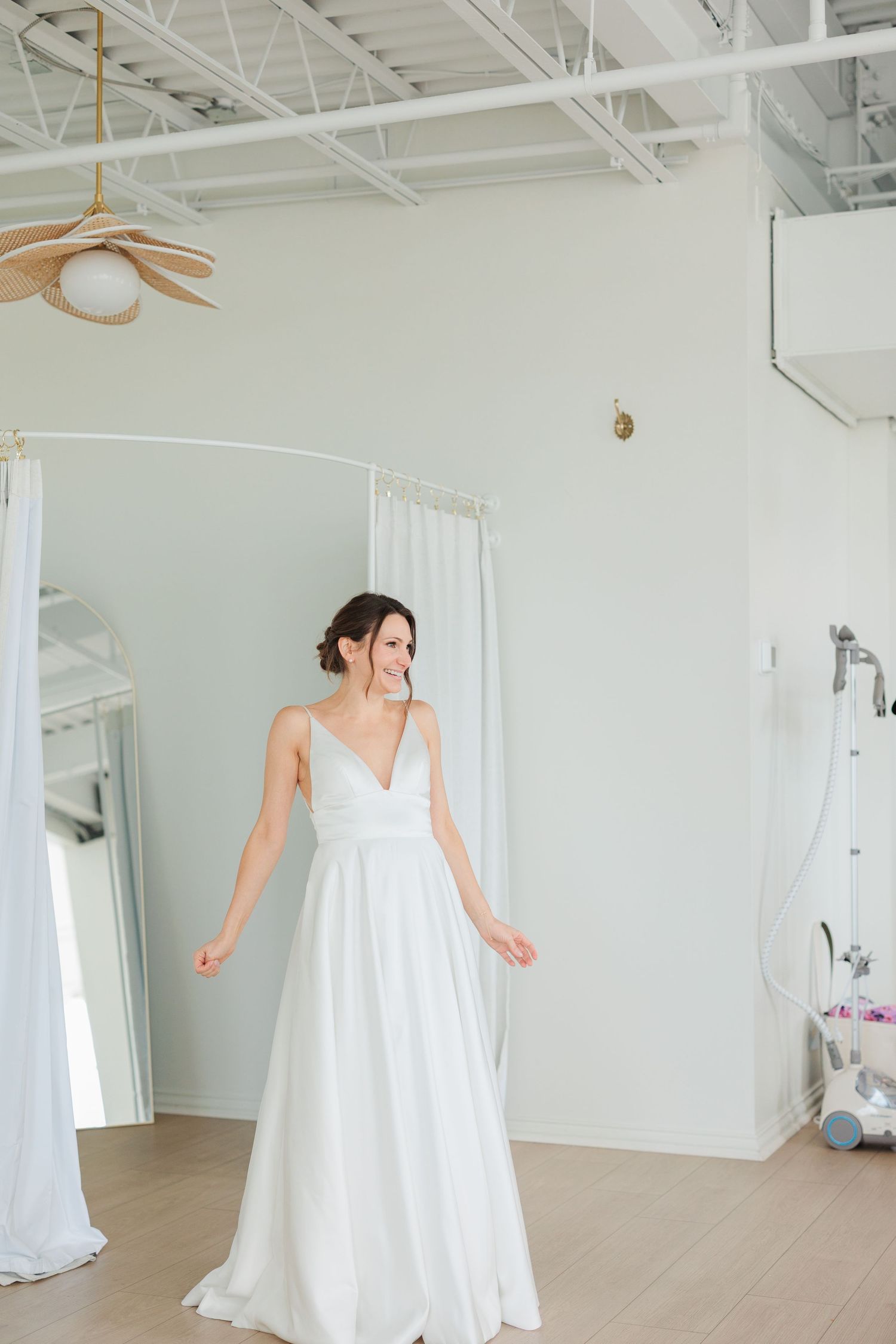 Bride in elegant white V-neck wedding gown twirling in a bright bridal boutique fitting room.