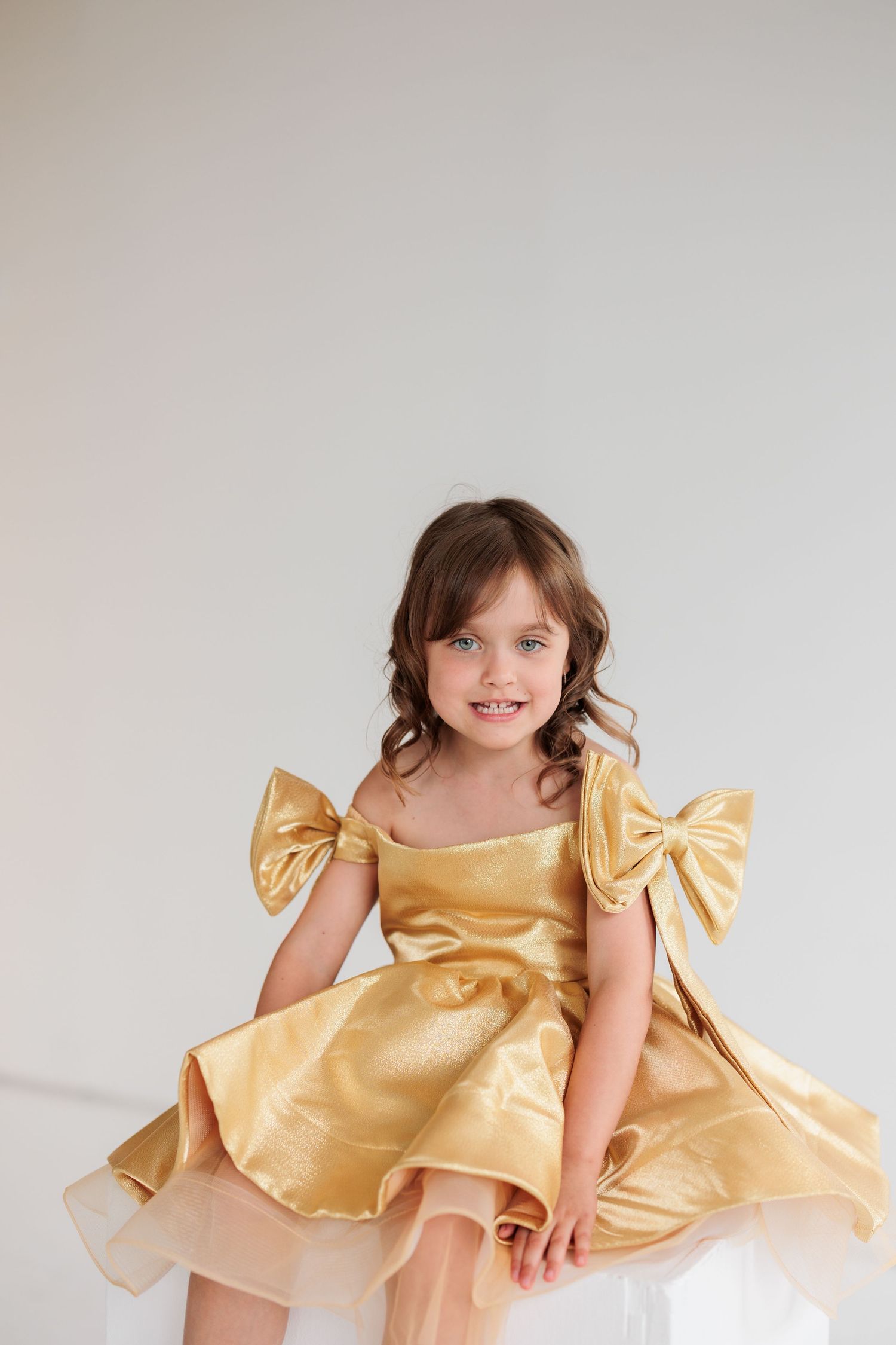 A young child twirls in a golden party dress with bow sleeves against a white background.

Rochester NY wedding photographer