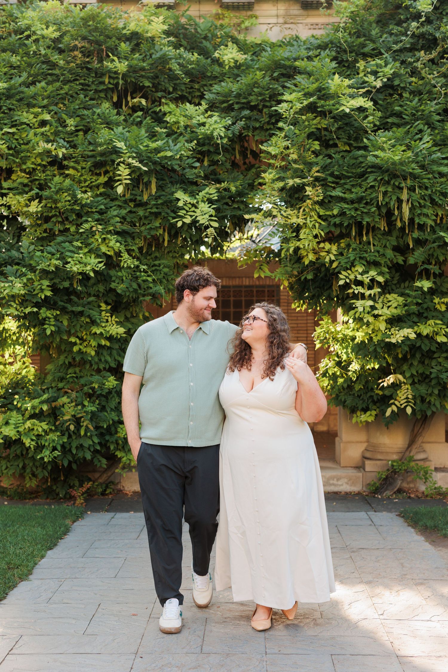 A couple sharing a joyful moment against a backdrop of green foliage and garden architecture.