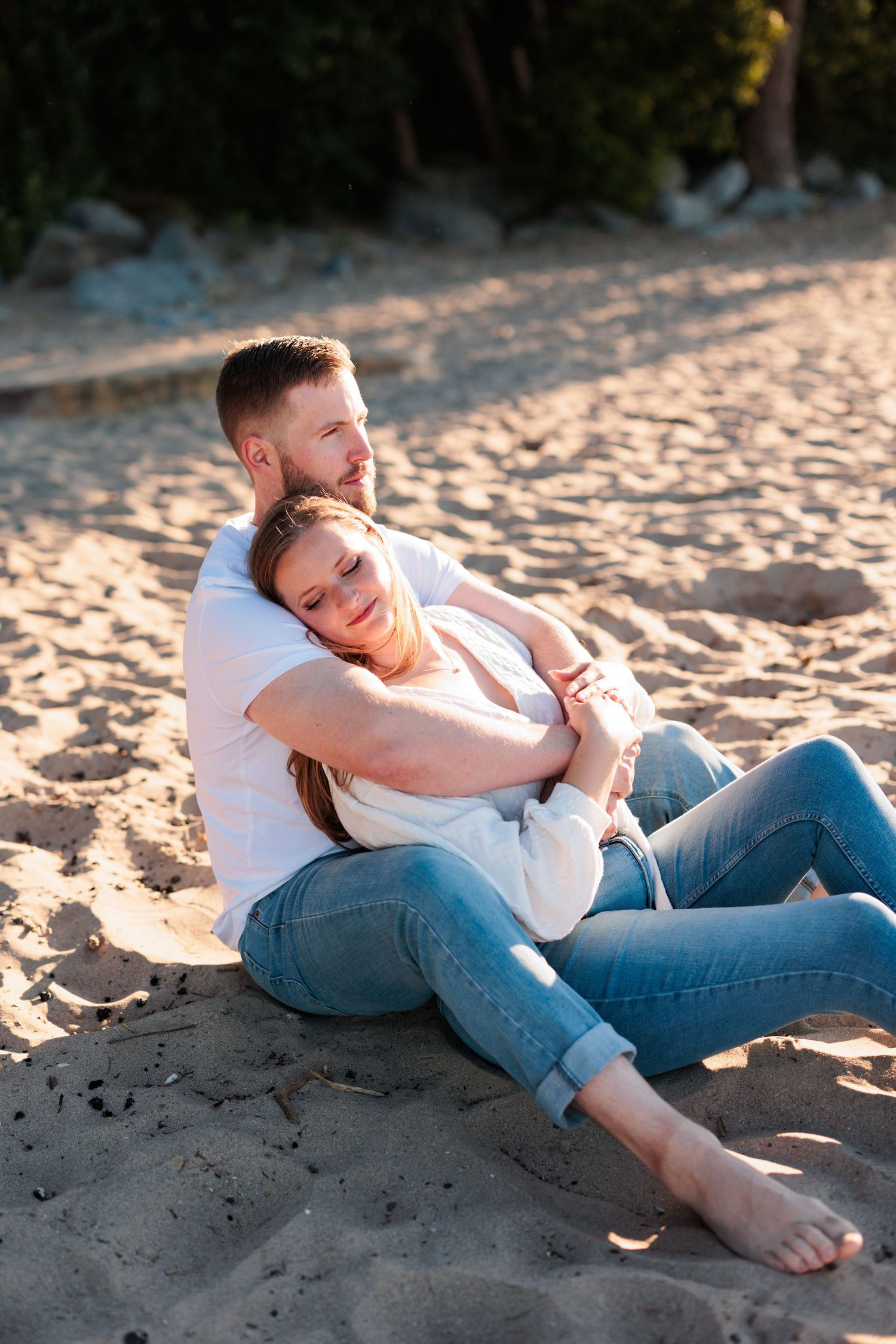 Couple relaxes together on sandy beach during intimate sunset photoshoot.