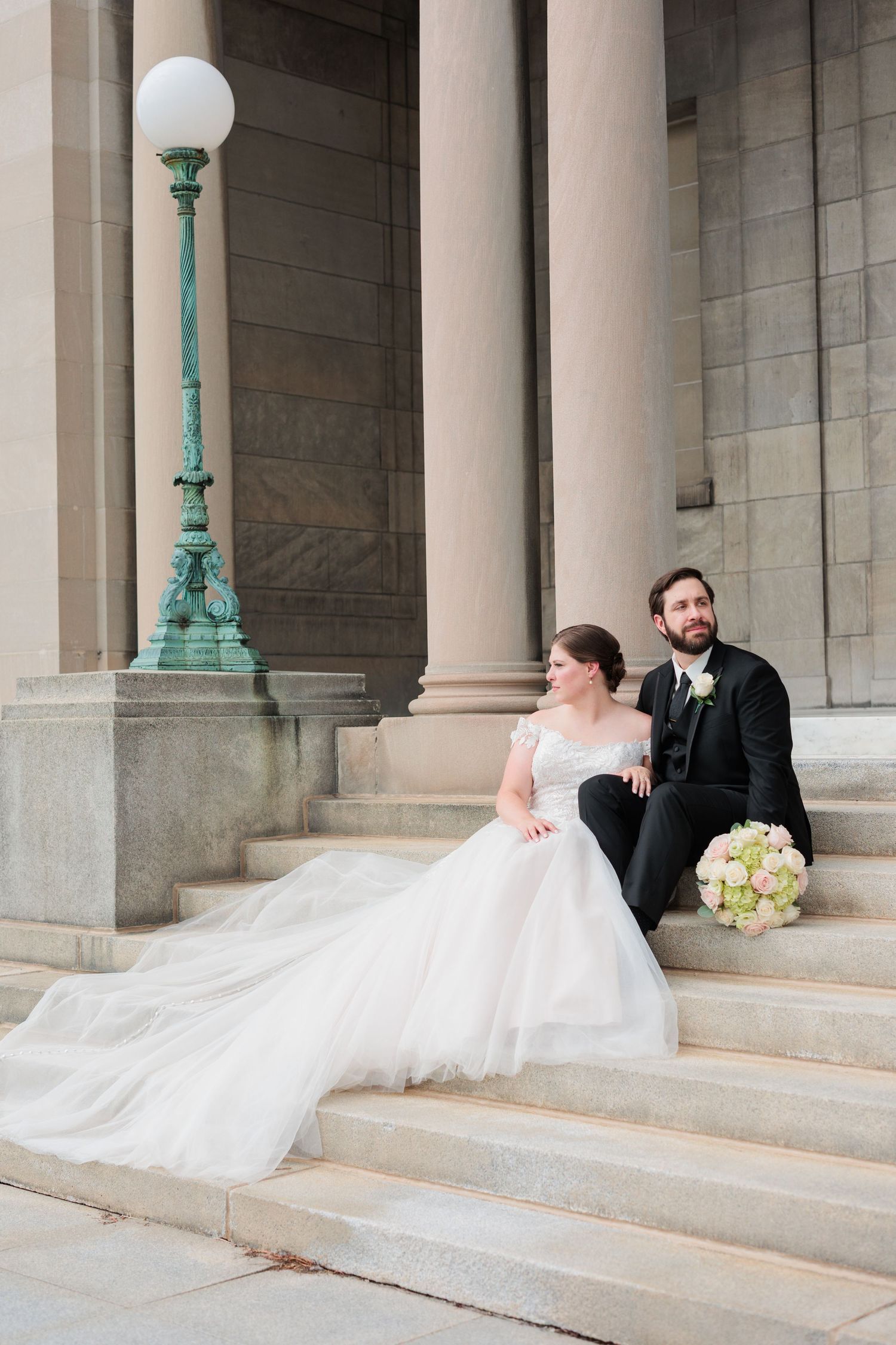 Wedding couple posing on grand stone steps with flowing veil.