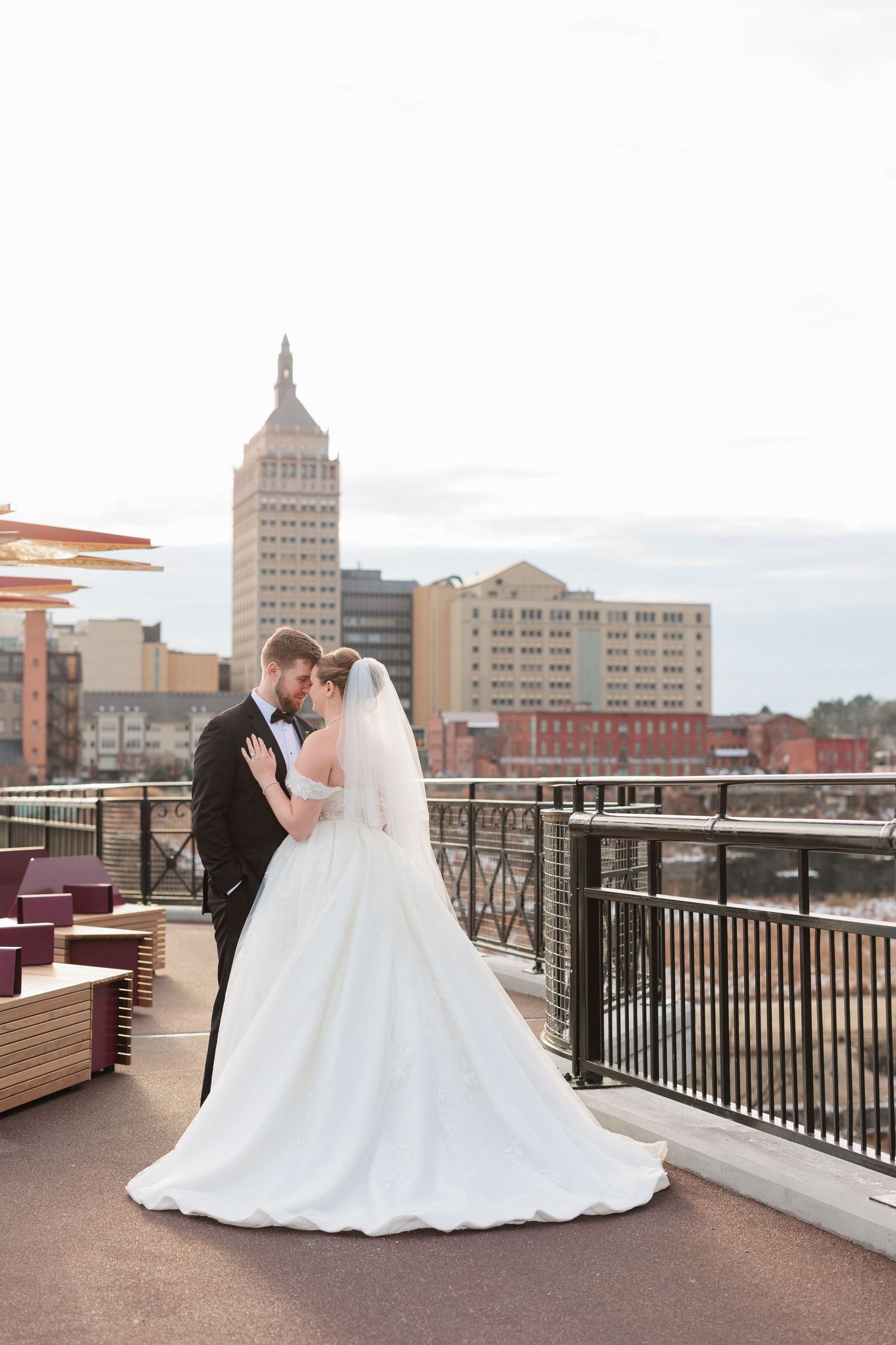 Wedding couple posing on urban rooftop with city skyline in background.