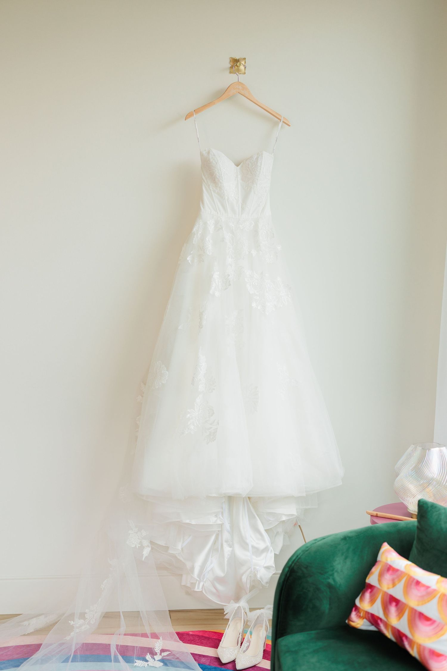 White wedding dress hanging on display against a neutral wall with green couch visible.