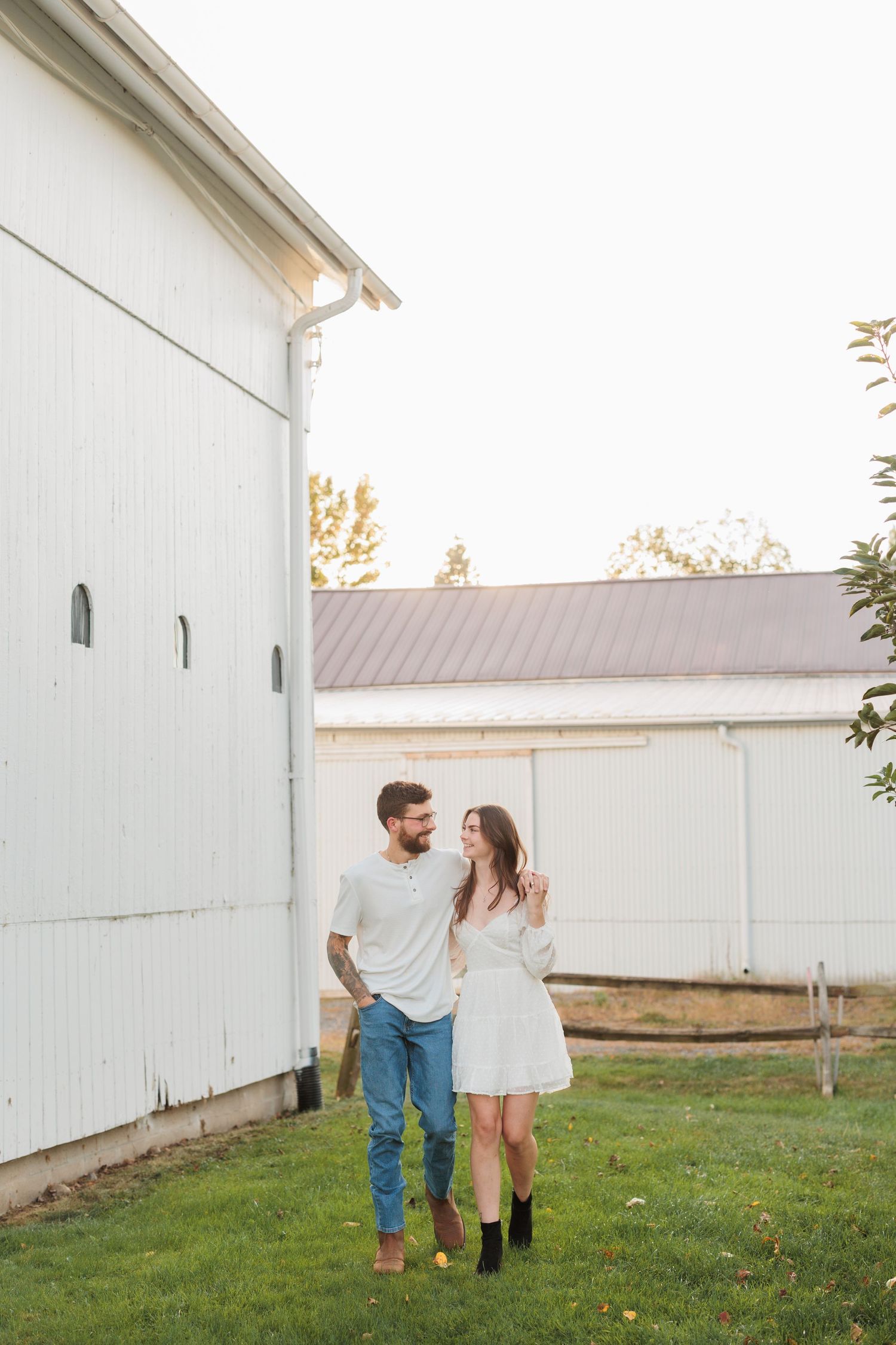 A couple in casual attire walks together on a grassy lawn beside a white building during sunset.