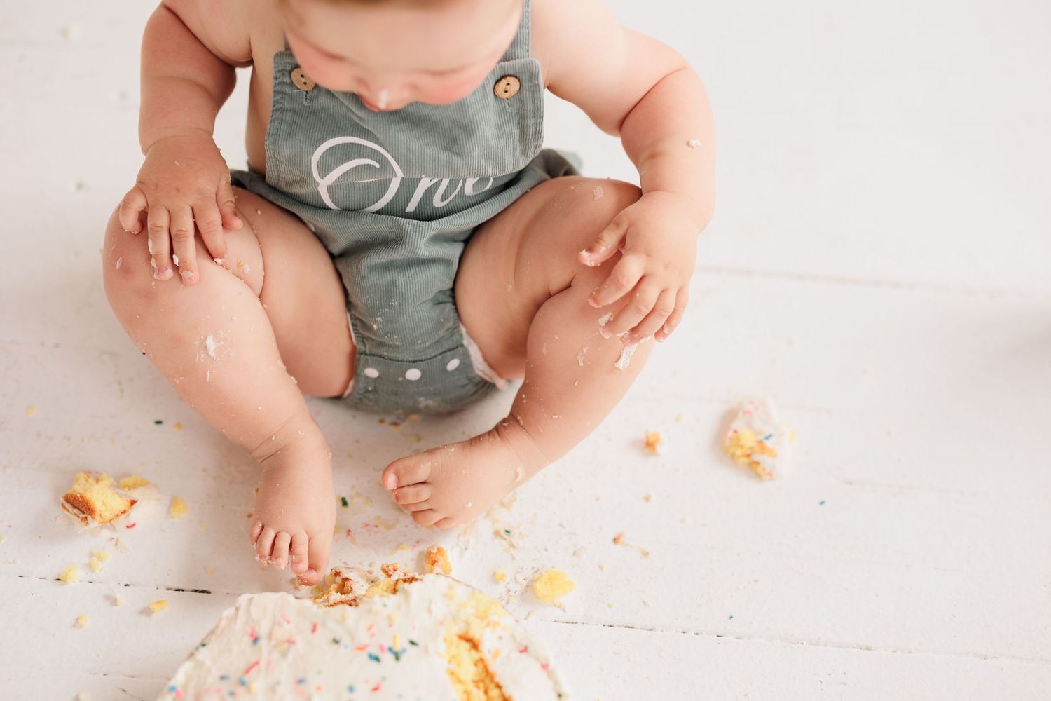 Baby's legs and torso shown sitting with cake crumbs scattered on white floor.

Rochester NY wedding photographer