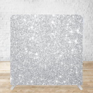 A silver glitter backdrop exhibiting a shimmering sparkly texture against a wooden floor and white brick wall.