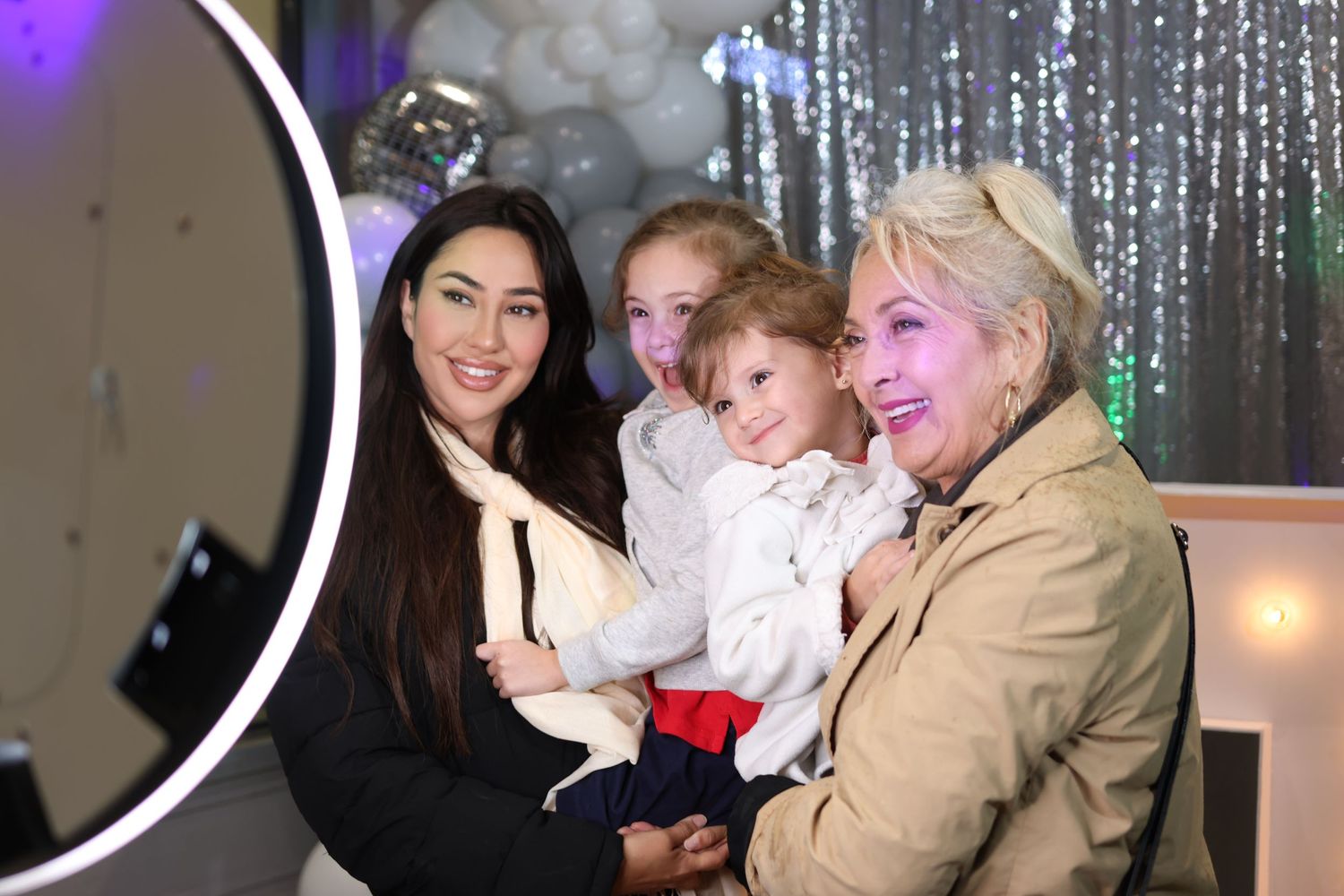 A group gathers around a photo booth backdrop with sparkly silver decorations.