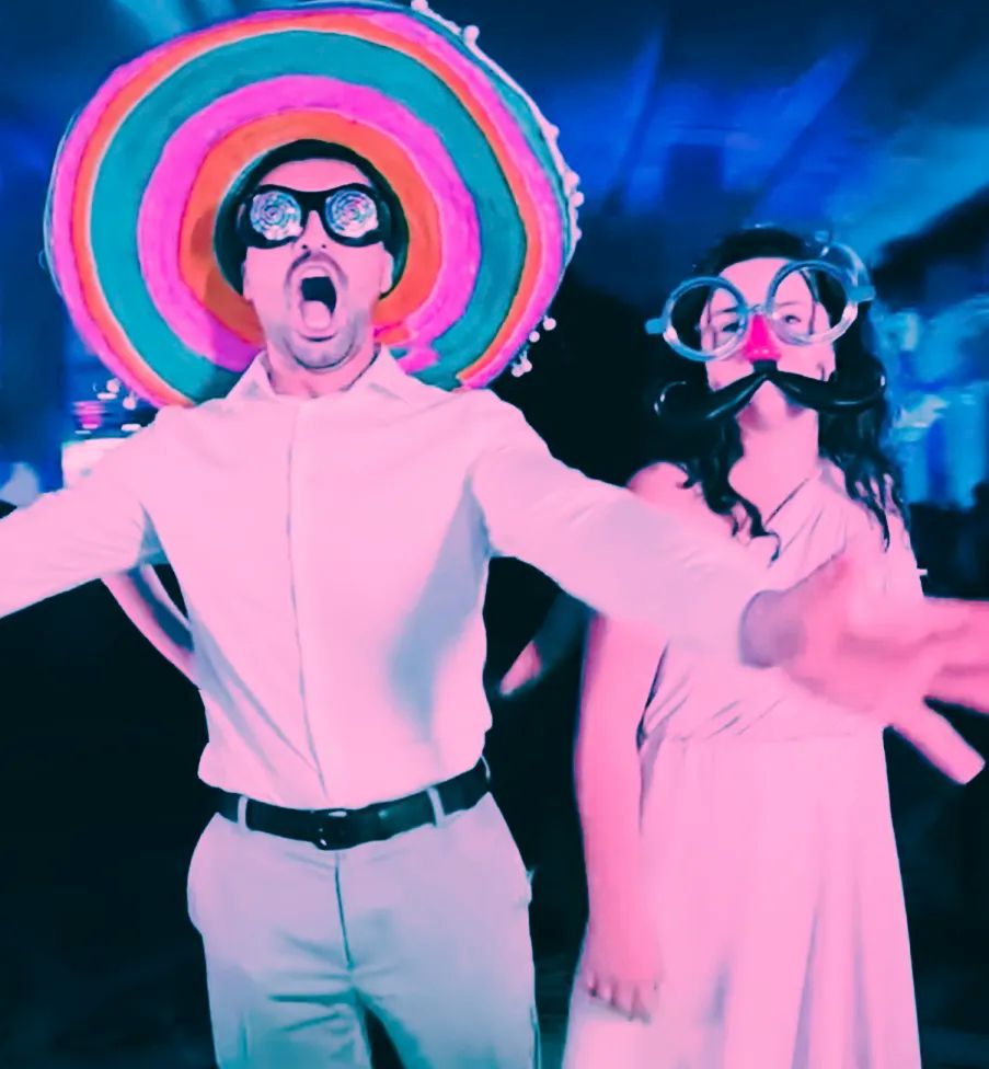 People in pink outfits dance and pose energetically against a blue-tinted background at a nighttime event.