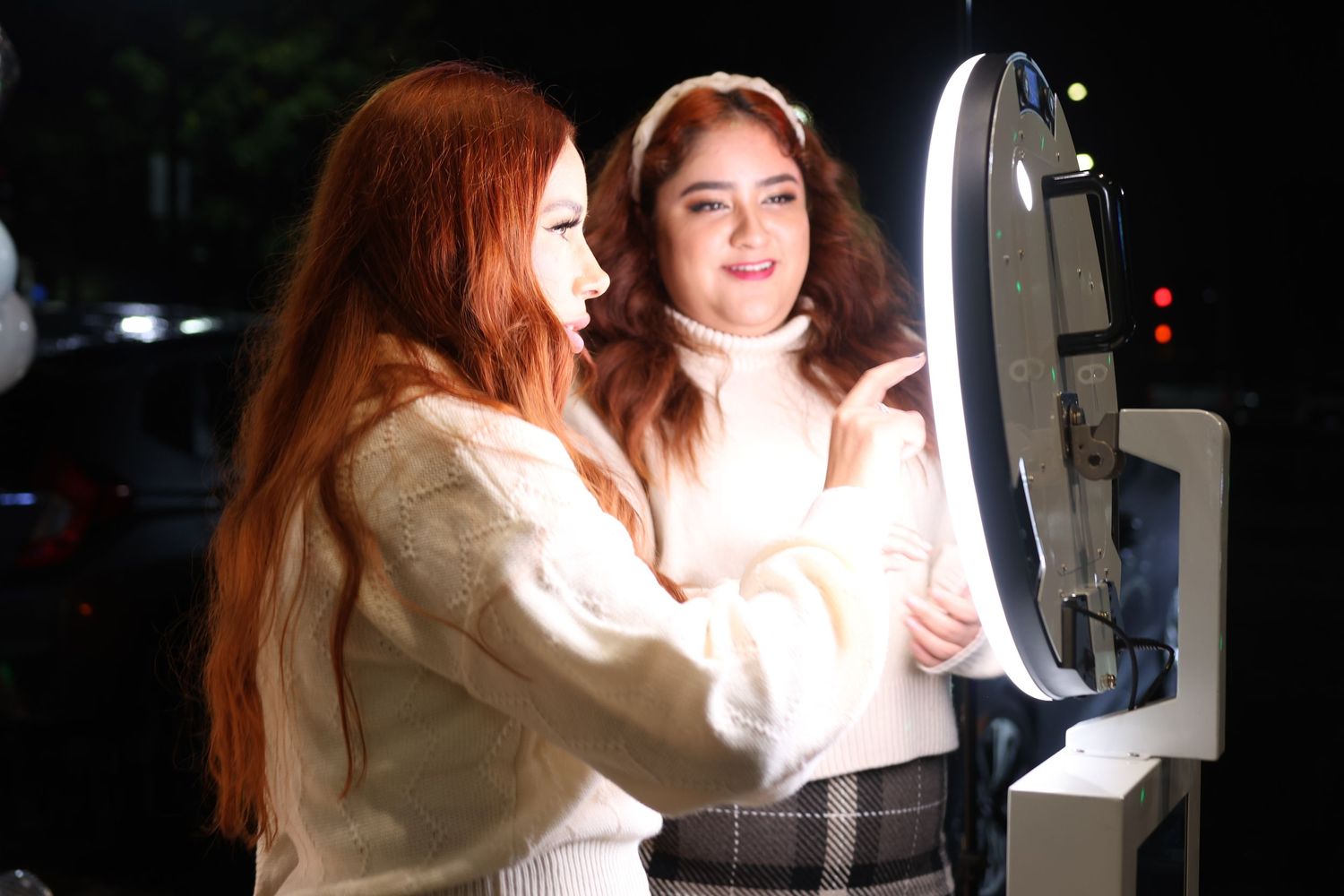 Two people looking at and interacting with a photo booth display in low light conditions.