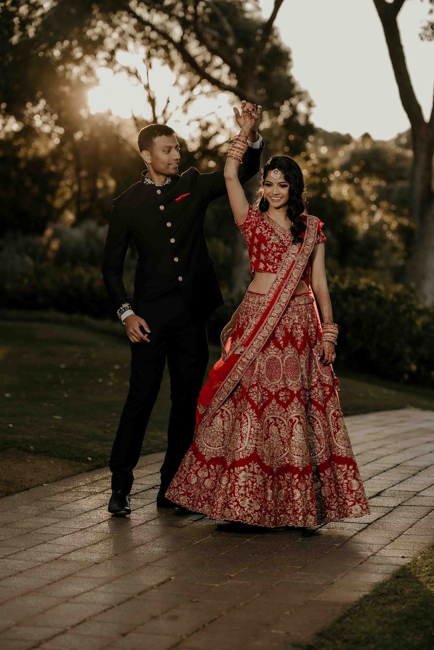 A couple in traditional Indian wedding attire dancing together at sunset.