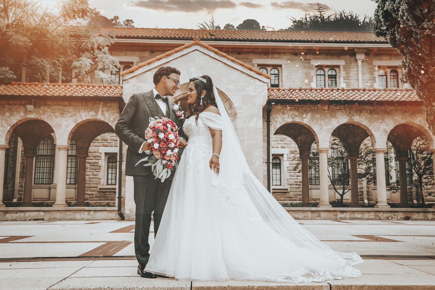 A romantic wedding portrait in front of a stunning Spanish colonial style building with arches at sunset.