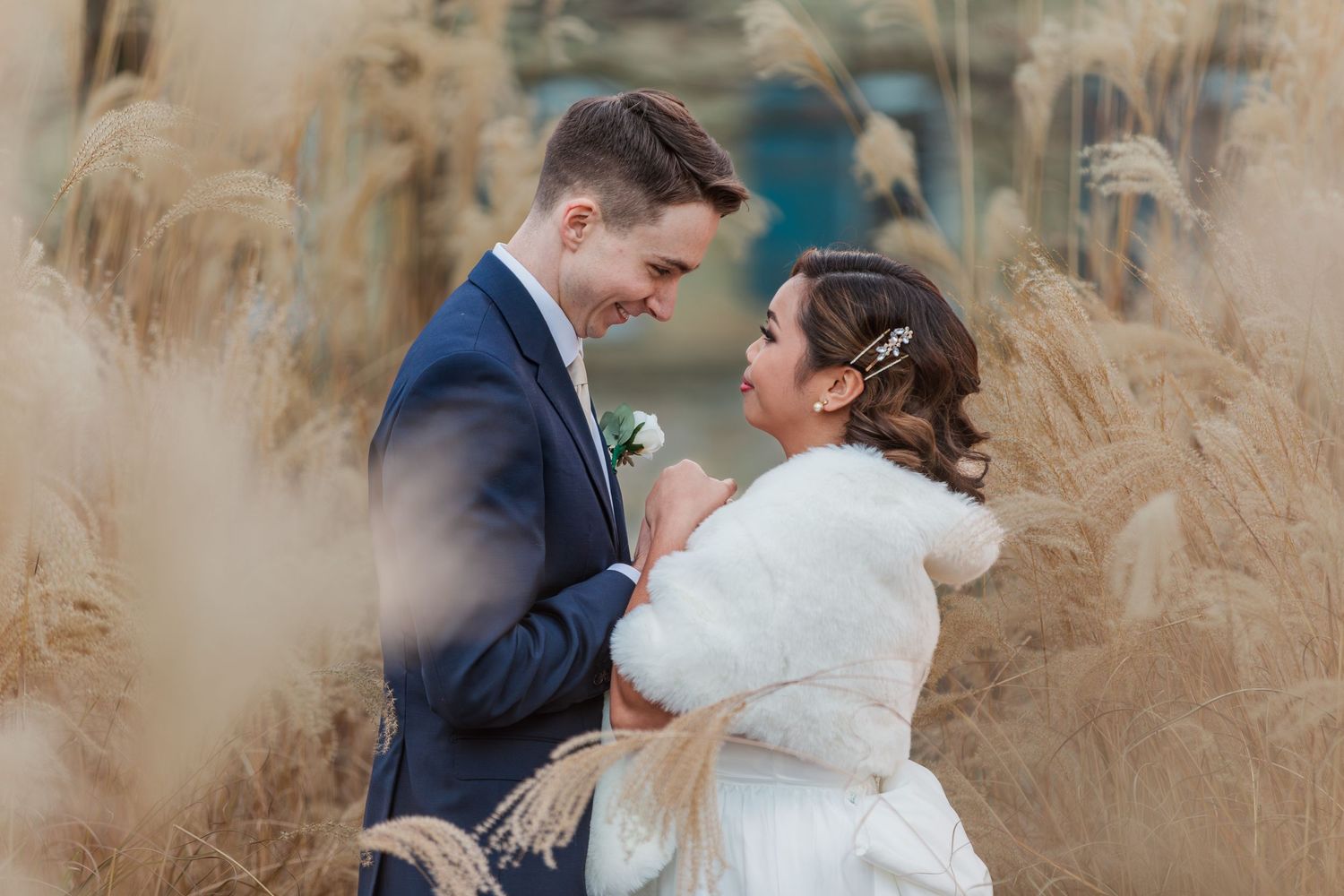 Bride and groom snuggling together to keep warm in the tall dead grass during their winter wedding in downtown Kitchener
