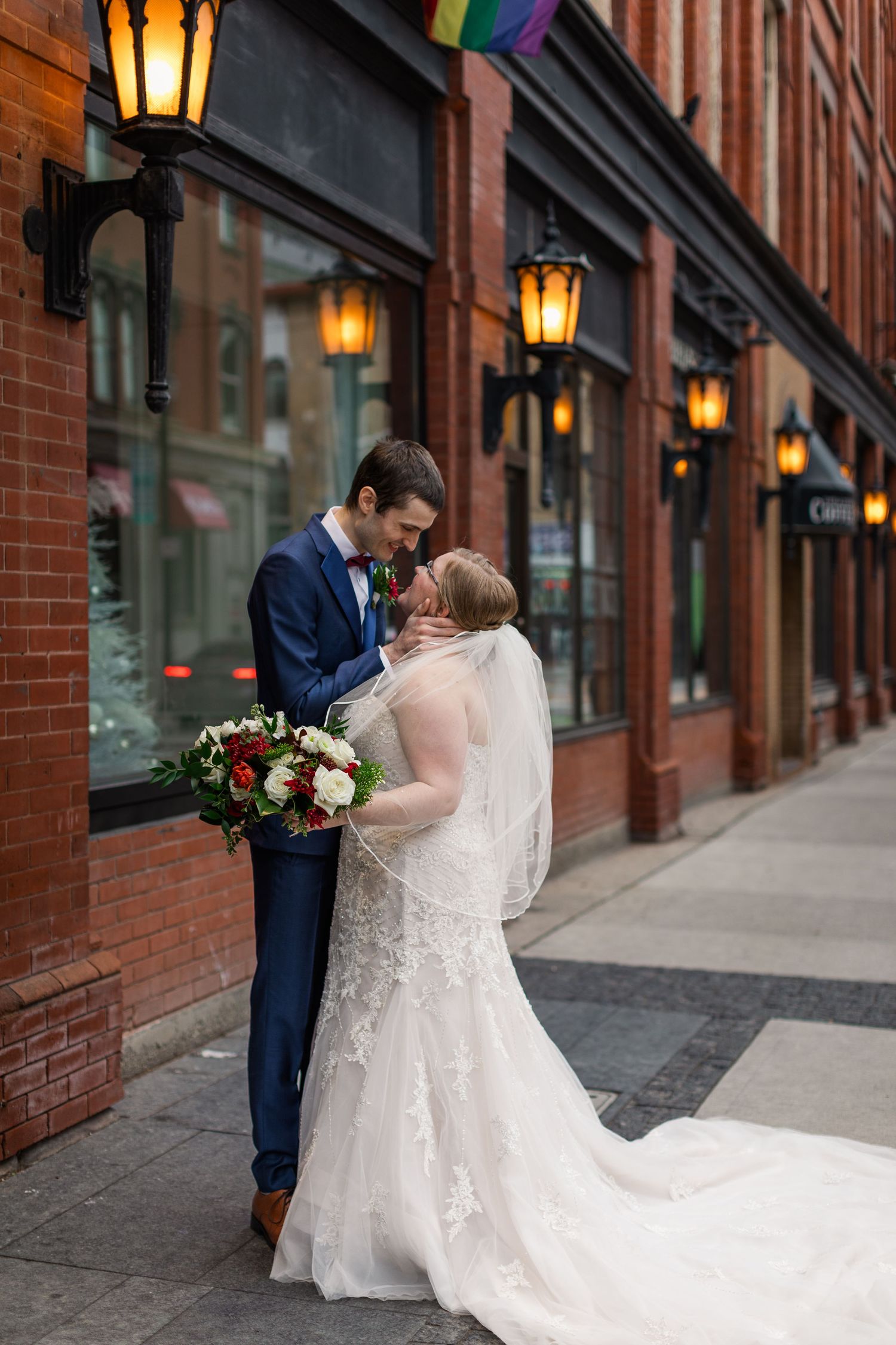 Candid wedding photography of groom pulling his bride in for a kiss on the street by the Walper Hotel in Downtown Kitchener, Ontario.
