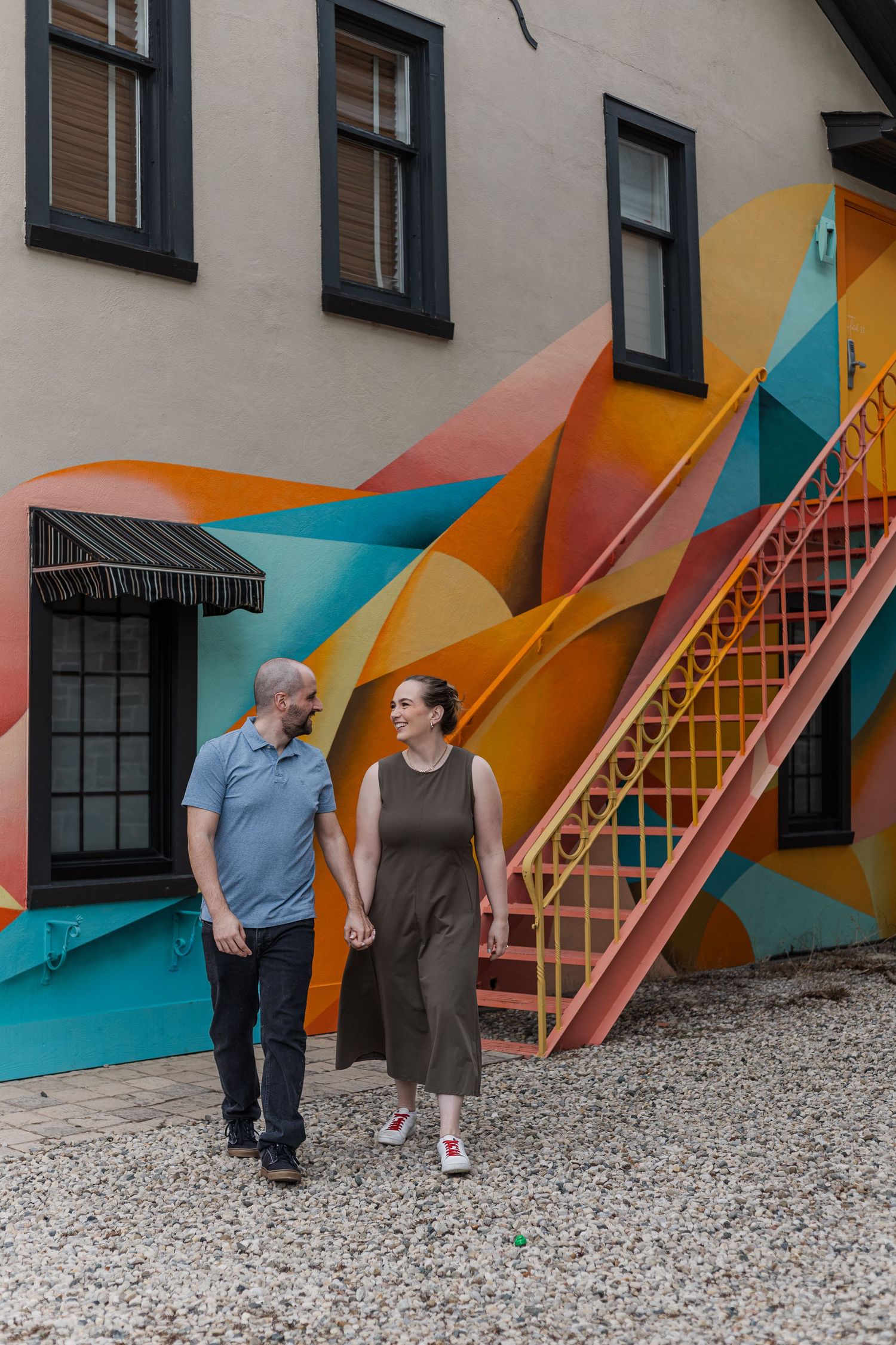 Couple look at each other while walking in front of a colourful geometric mural on a wall in downtown St. Jacobs, Ontairo.