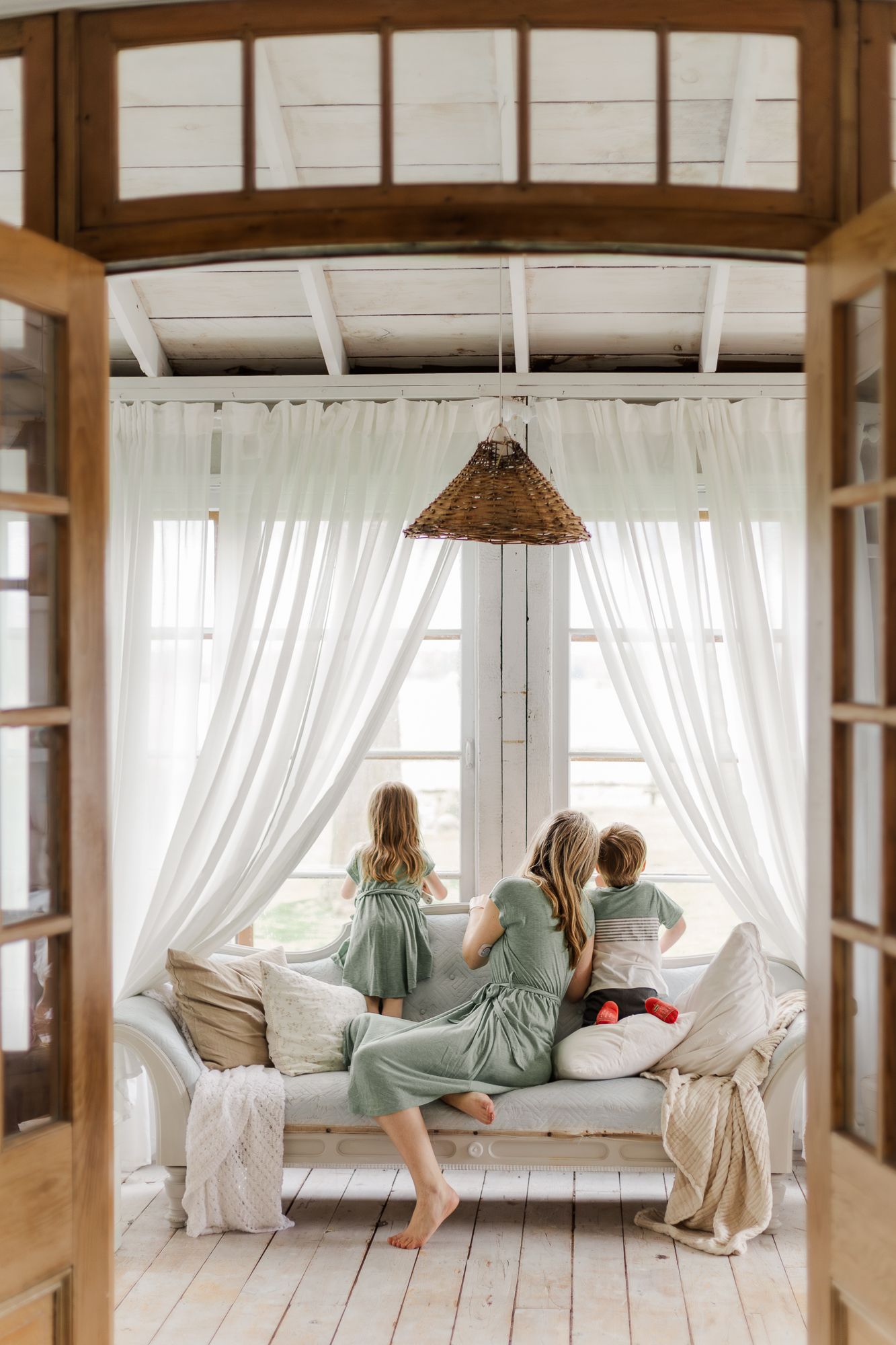 A mother sitting on a vintage couch with her two kids looking out the window of the sunroom at the animals outside in waterford ontario.