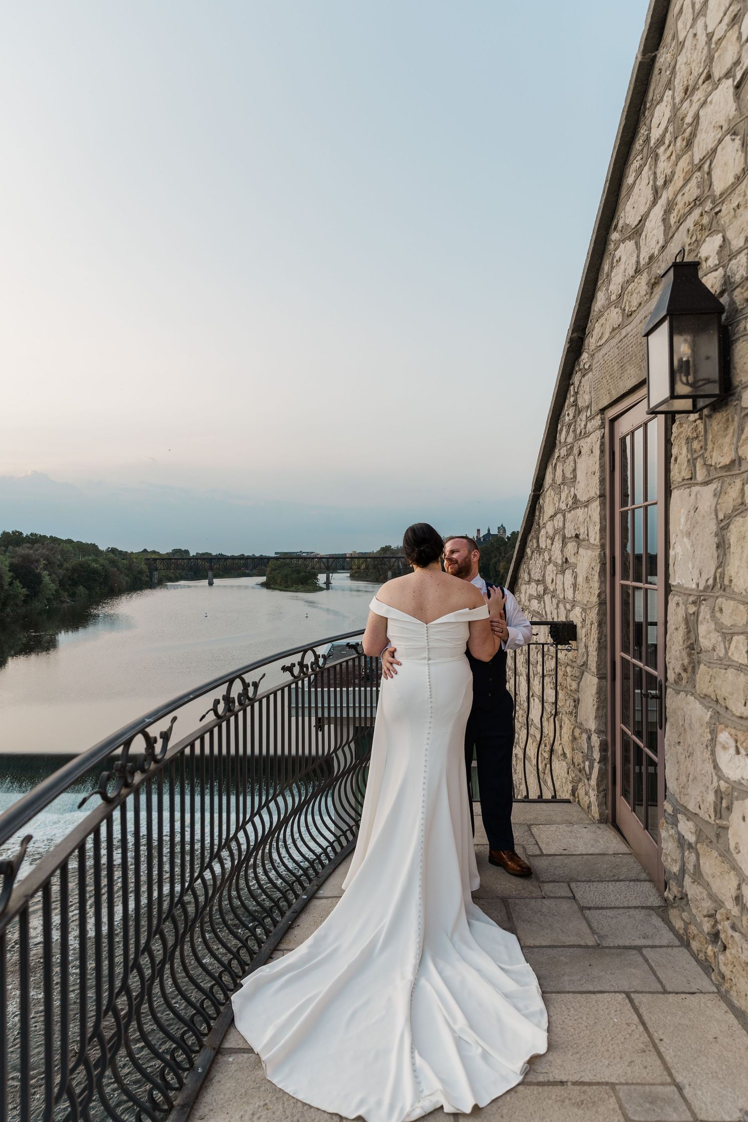 Wedding photography of bride and groom share a quiet moment on balcony over looking a river at the Cambridge Mill in Cambridge, Ontario.
