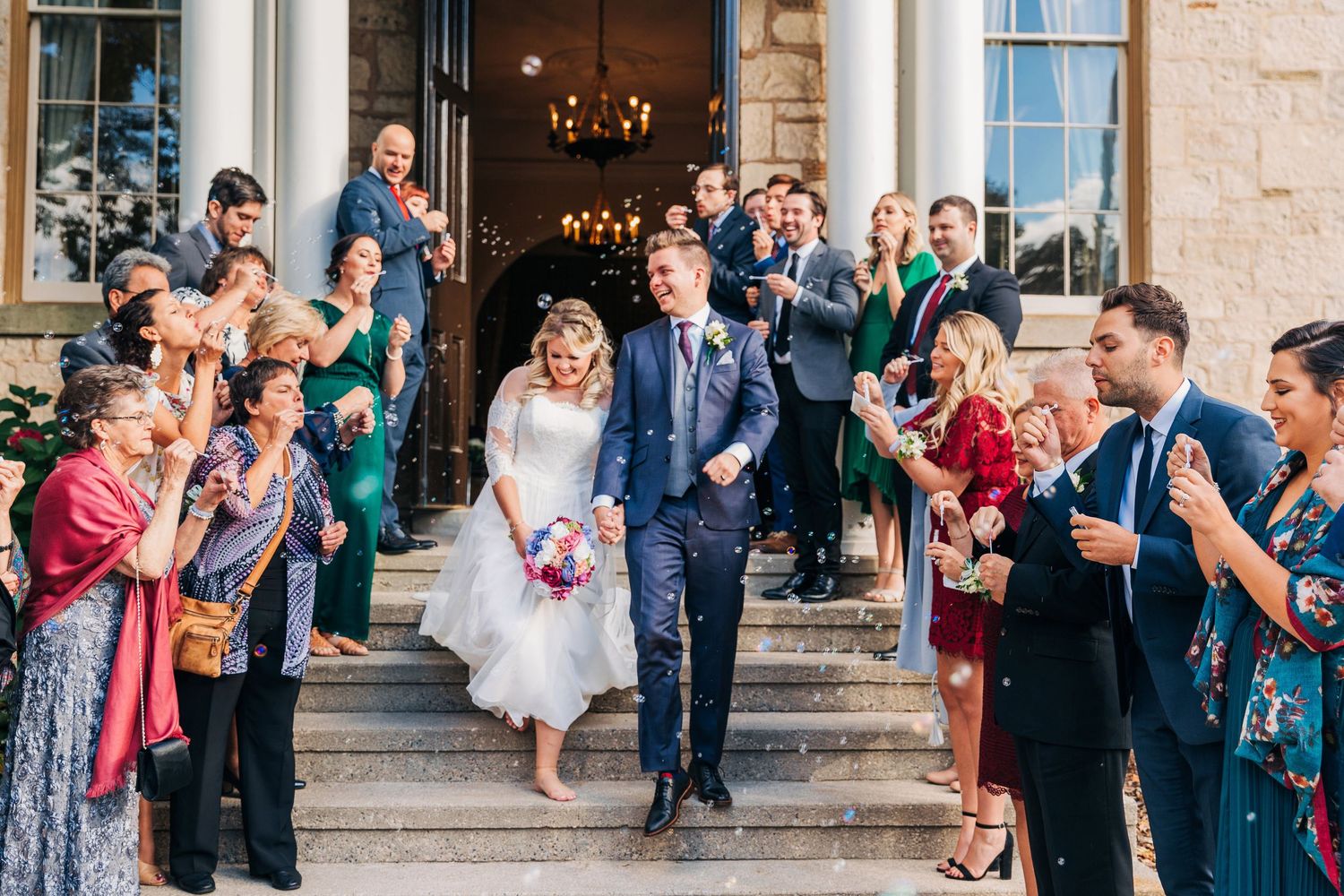 Candid wedding photo of bride and groom exiting the ancaster old town hall with their guest blowing bubbles in ancaster, ontario.