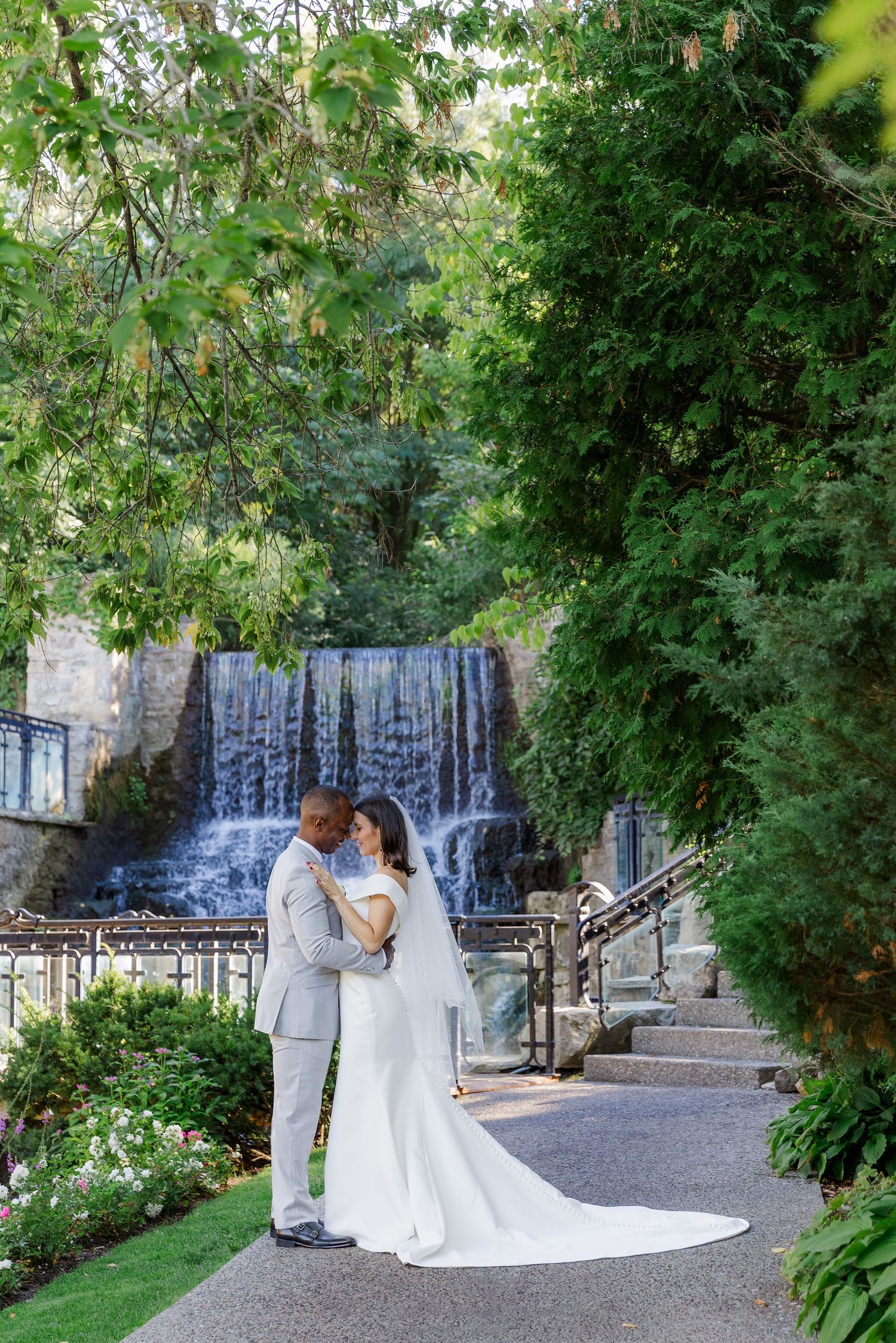 Calm wedding photo of bride and groom snuggled close together in front of the waterfall at ancaster mill in ancaster, ontario.