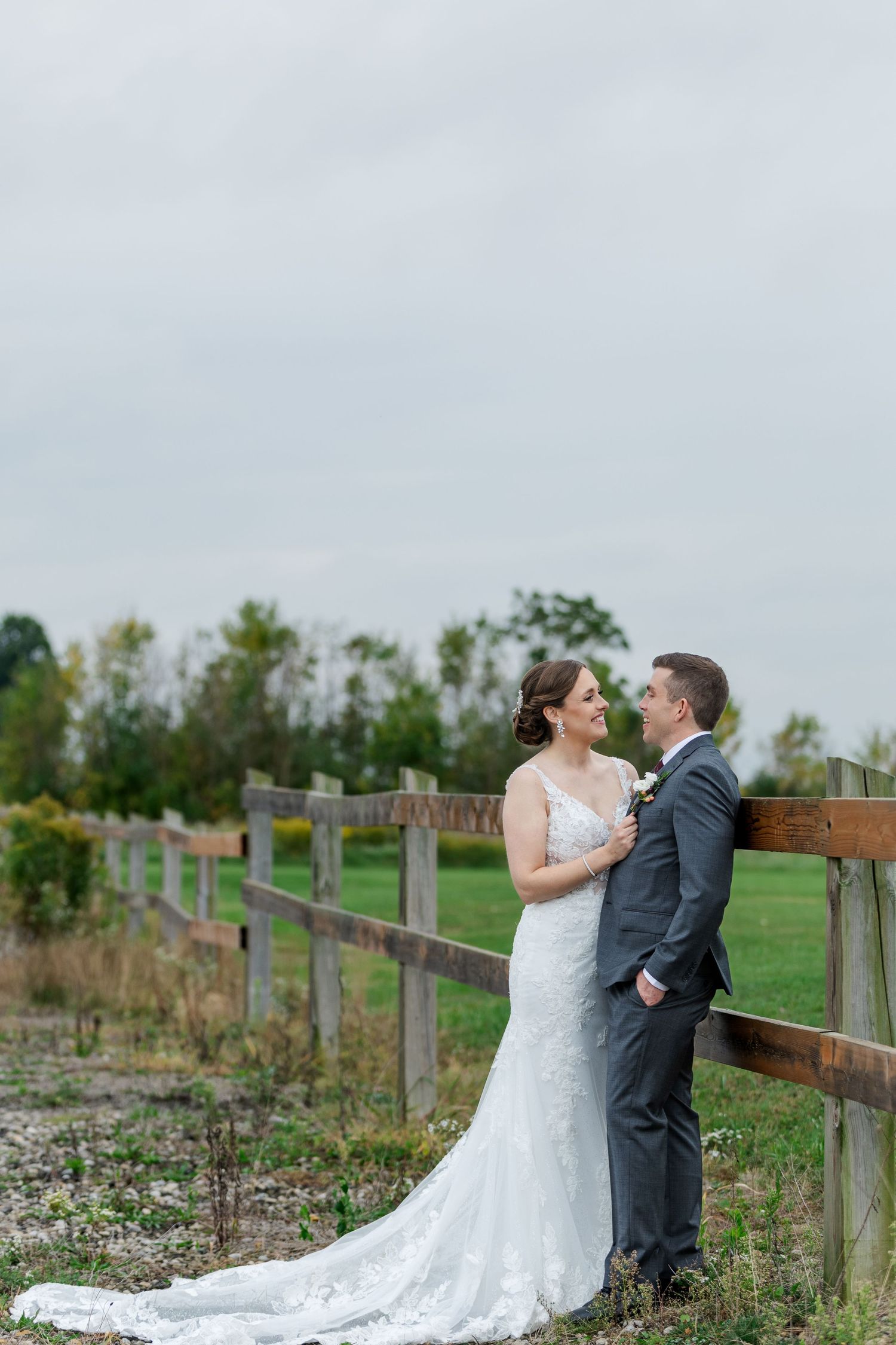 Calm wedding photo of bride and groom leaning against a wooden fence in a field near woodstock, ontario.