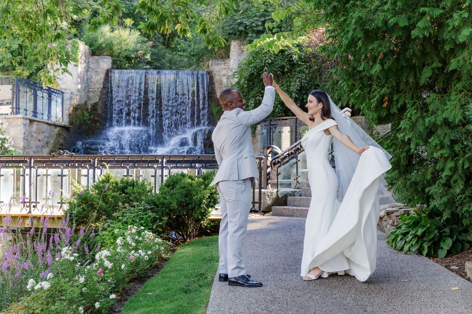 Natural wedding photography of bride and groom twirling in front of the waterfall at the ancaster mill in ancaster, ontario.
