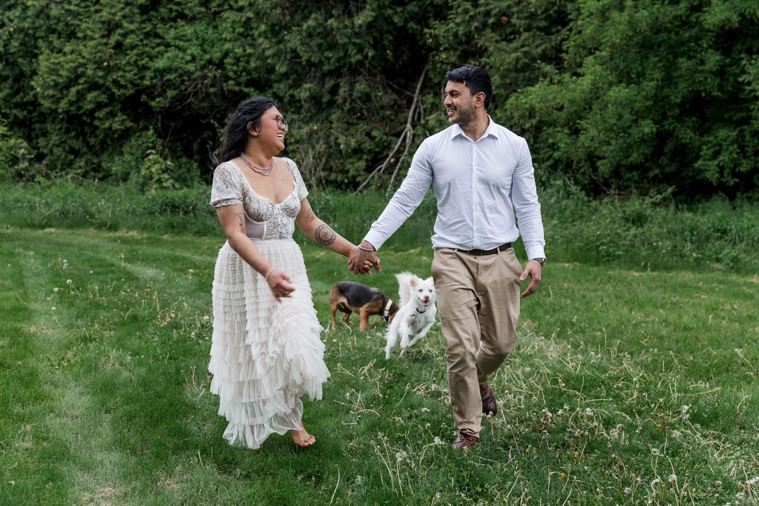 Candid engagement photo of couple running through a field with their dogs at the guelph arboretum.